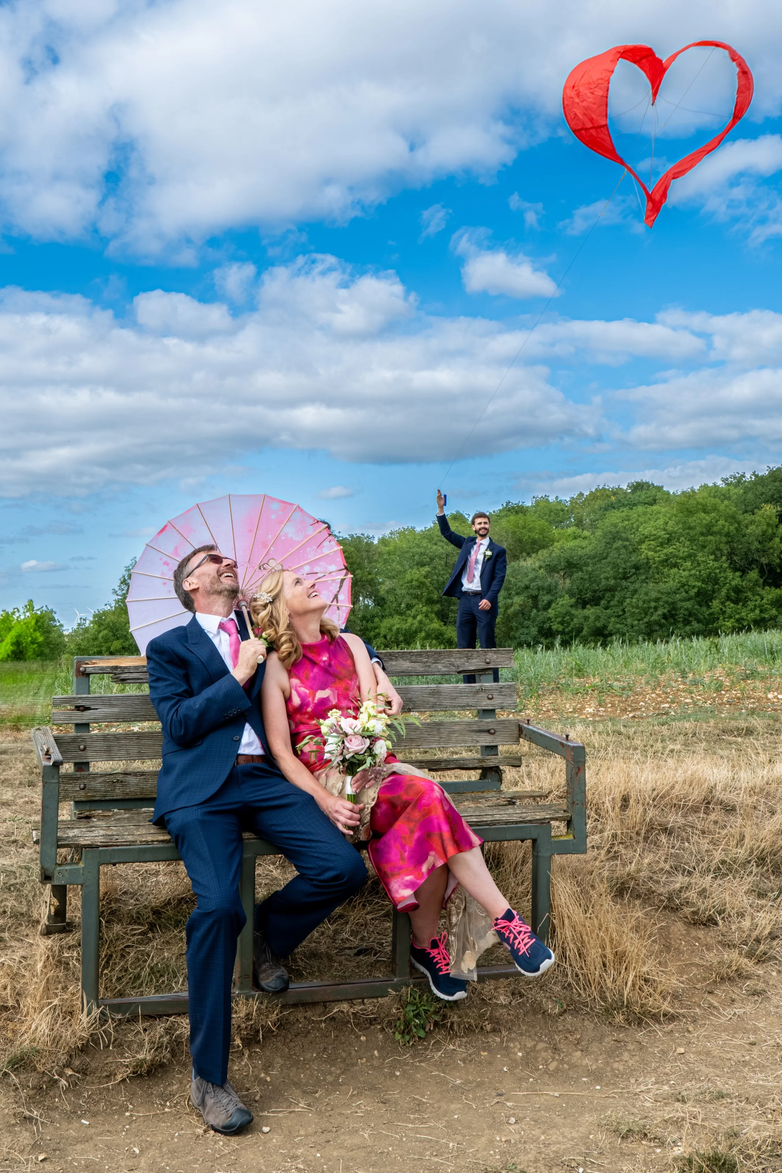 Bride and groom with a heart shaped kite, photographed naturally outdoors.