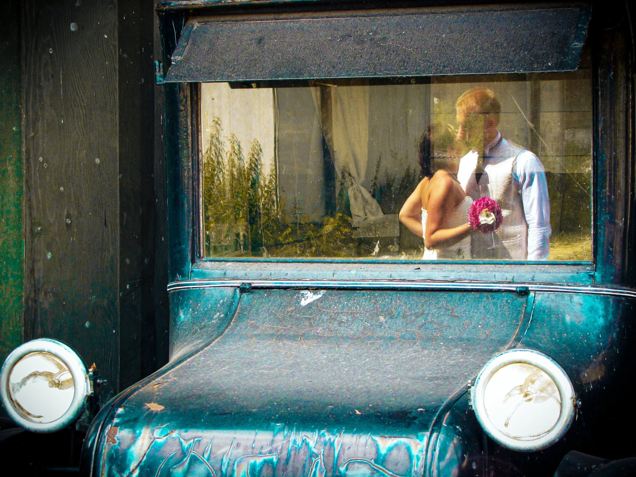 Wedding couple photographed in the reflection of a classic car, an example of candid wedding photography.