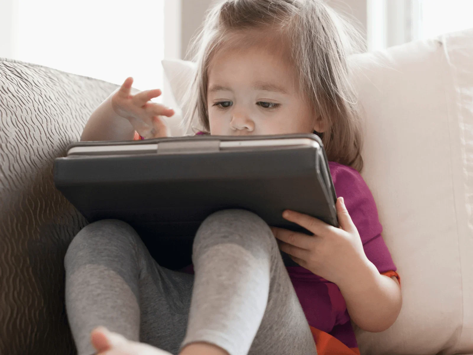 Young child sitting on couch playing on an ipad or tablet