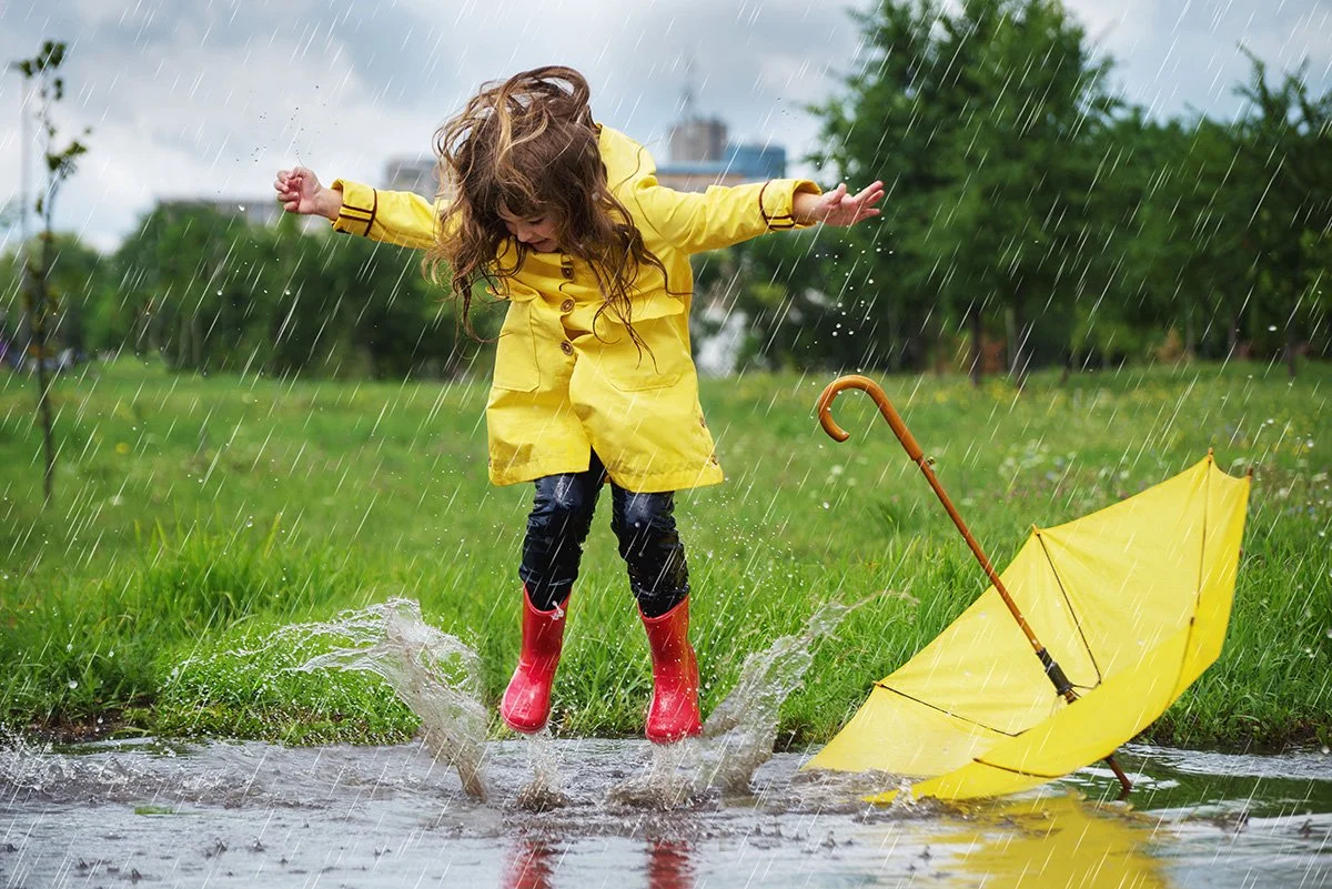 child playing in rain puddle with raincoat and umbrella on rainy day