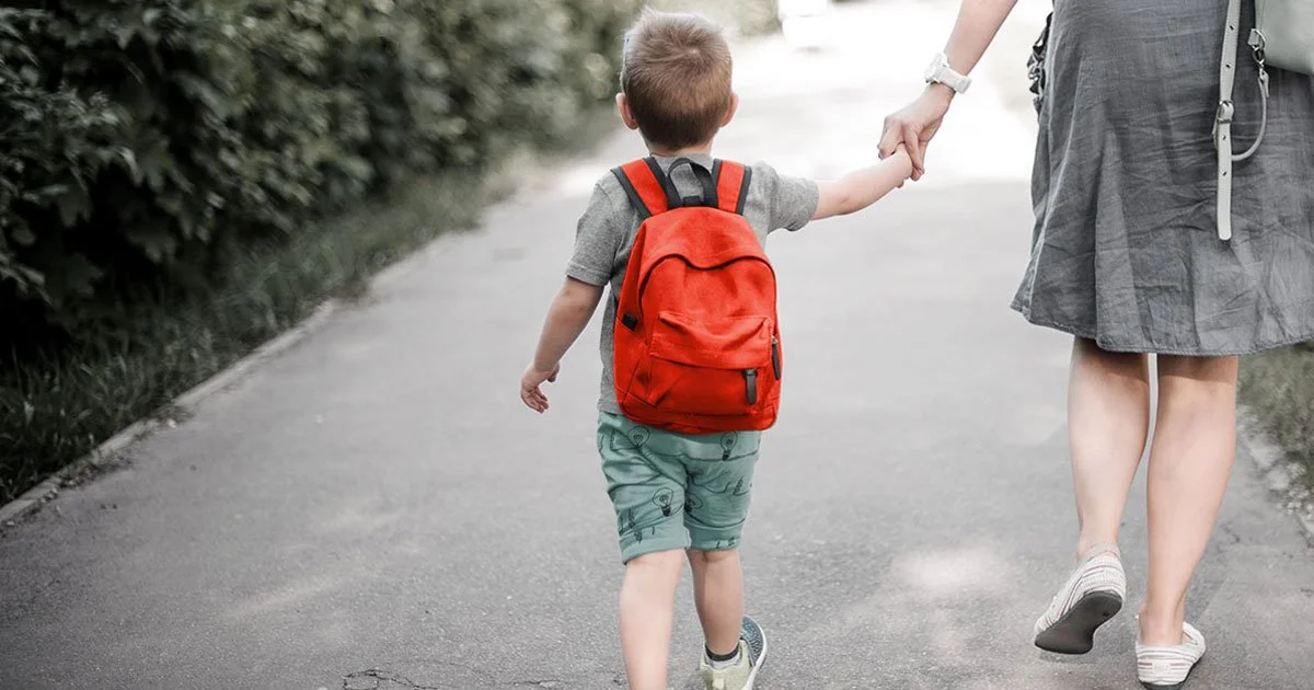 little boy walking with his mom and wearing a bookbag for school