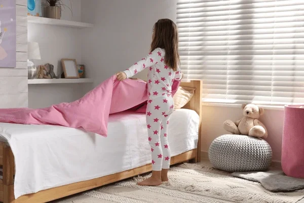 little girl making her bed in her room