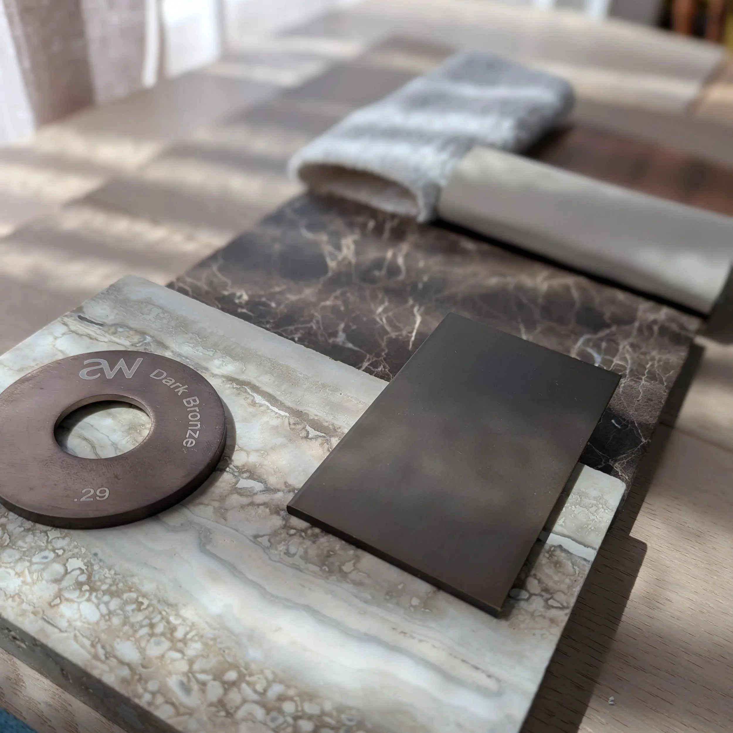 Samples of marble and tile finishes, including a dark bronze-colored circular sample, rectangular tile, and various marble slabs with different colors and patterns, on a wooden surface.