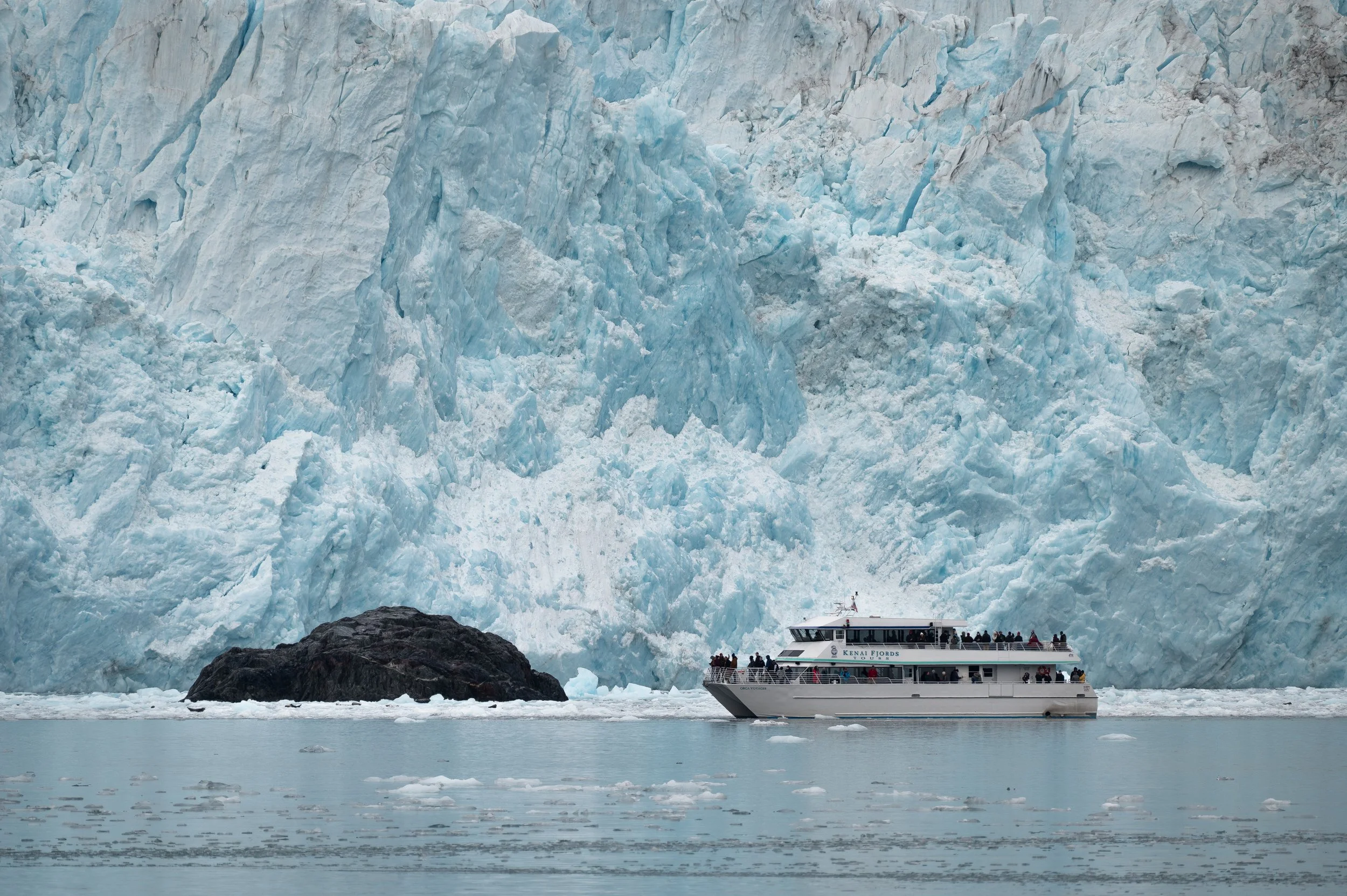 Tour boat approaches a massive glacier in Alaska with icy waters and icebergs floating nearby.