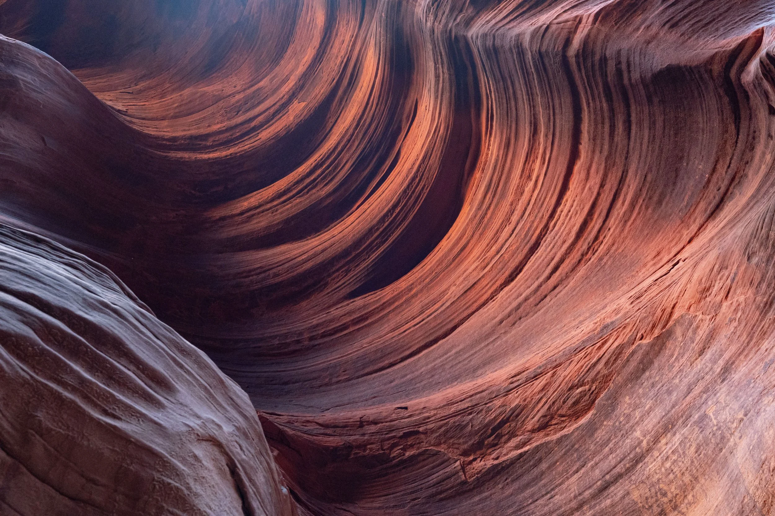 Curved sandstone formations with layered textures, showcasing vibrant red and orange hues, resembling Antelope Canyon.