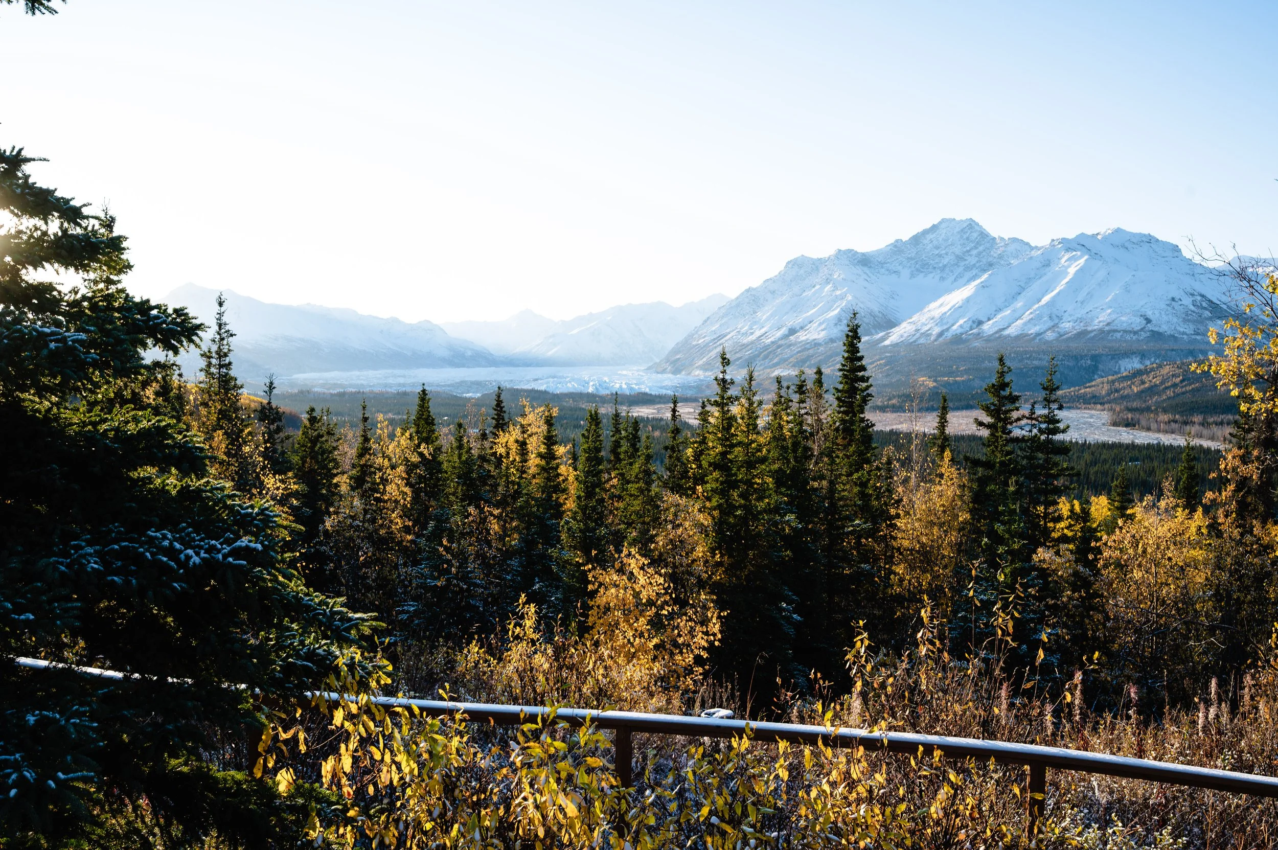 Mountain landscape with snow-covered peaks, evergreen trees, and autumn foliage.