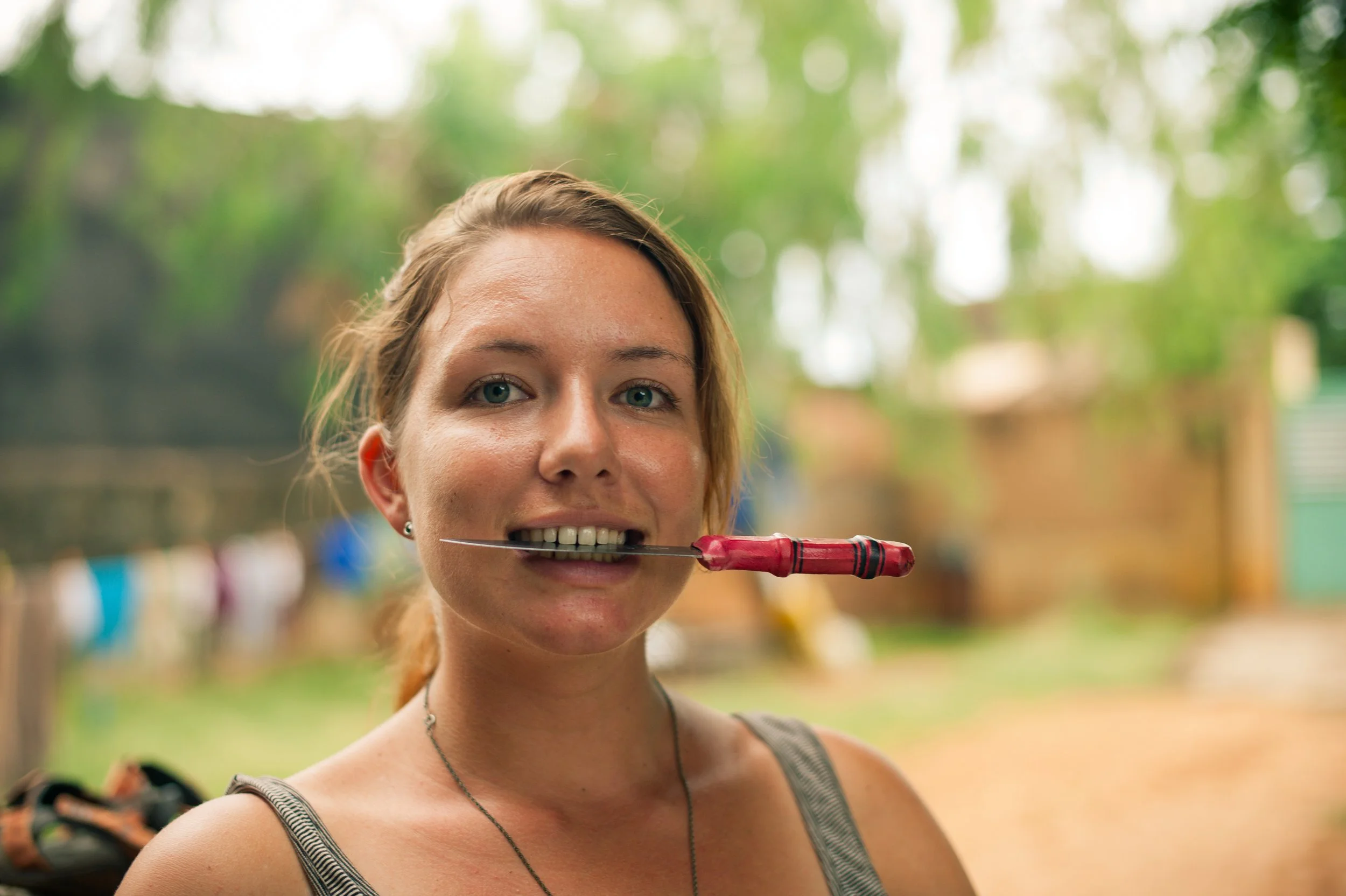 Woman holding a knife with a red handle in her mouth outdoors.