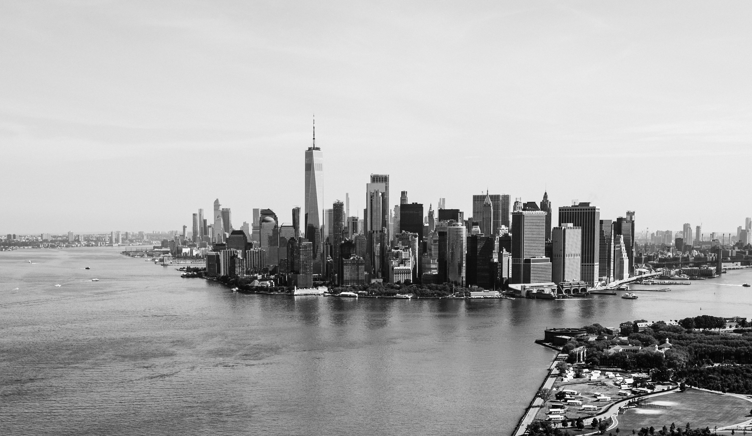 Black and white aerial view of New York City skyline with skyscrapers and waterfront.