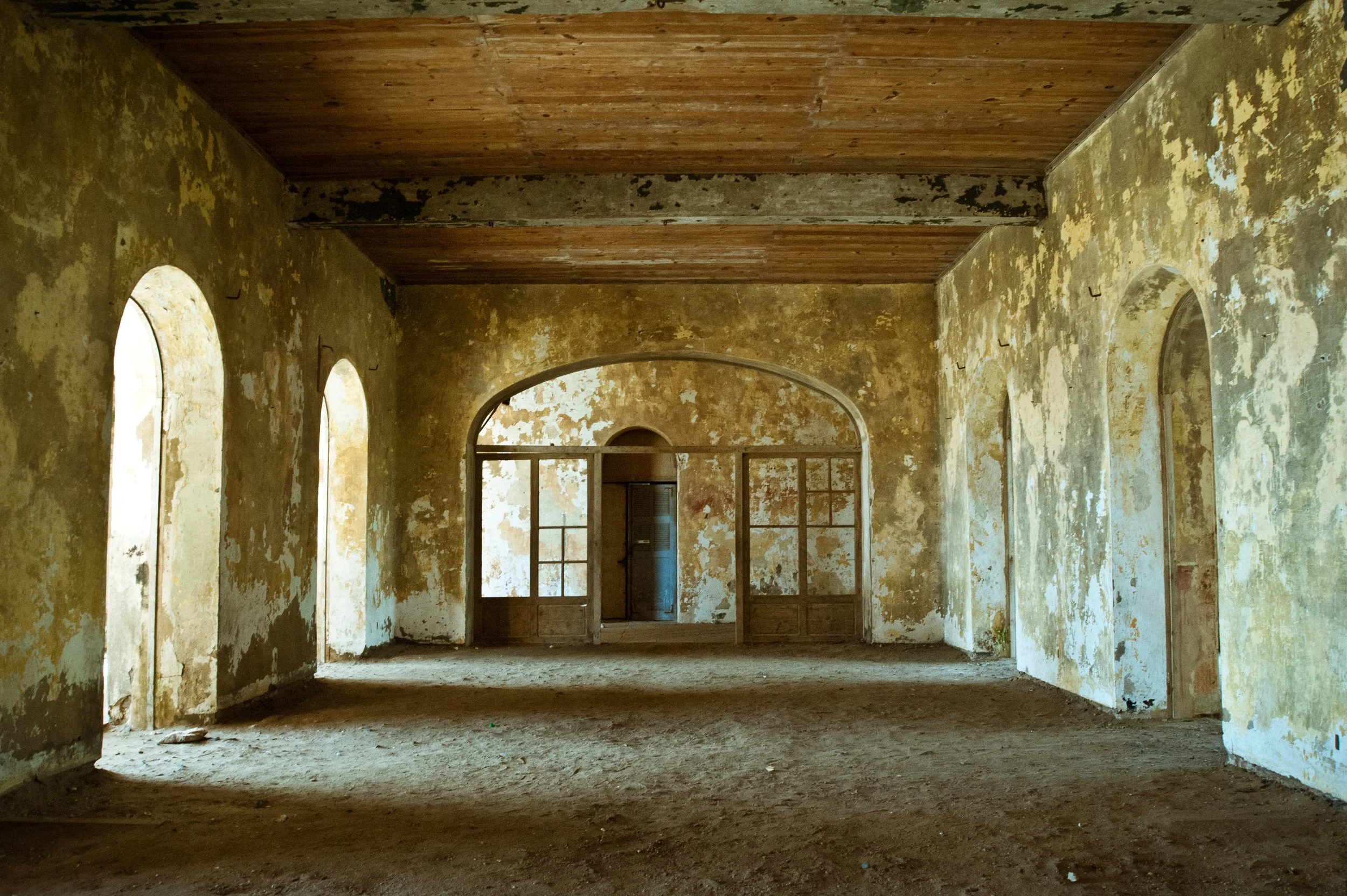 Abandoned room with arched windows, weathered walls, and a wooden ceiling.