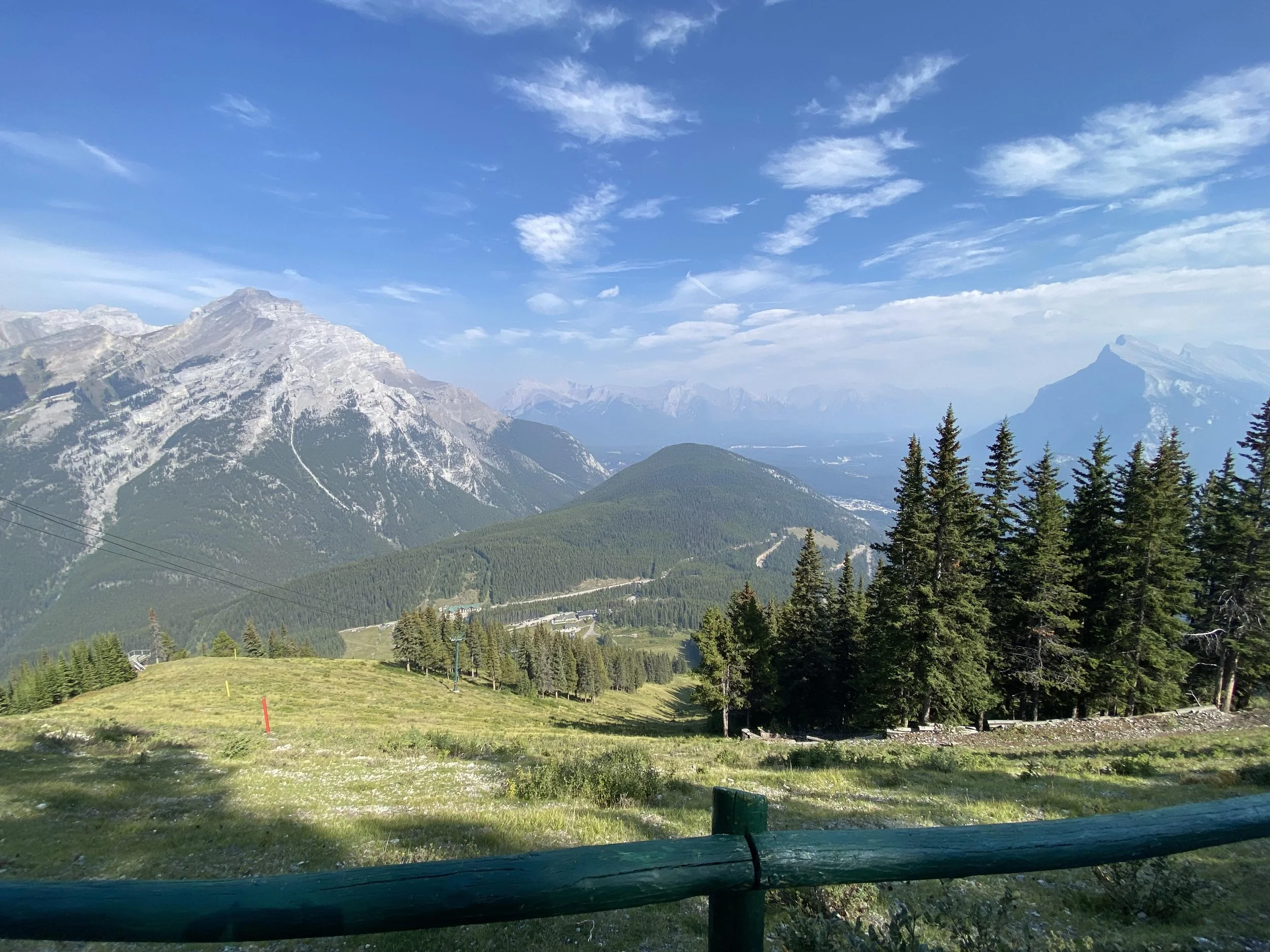 The view from a trail of a series of lush hills fading into a mountainous backdrop.