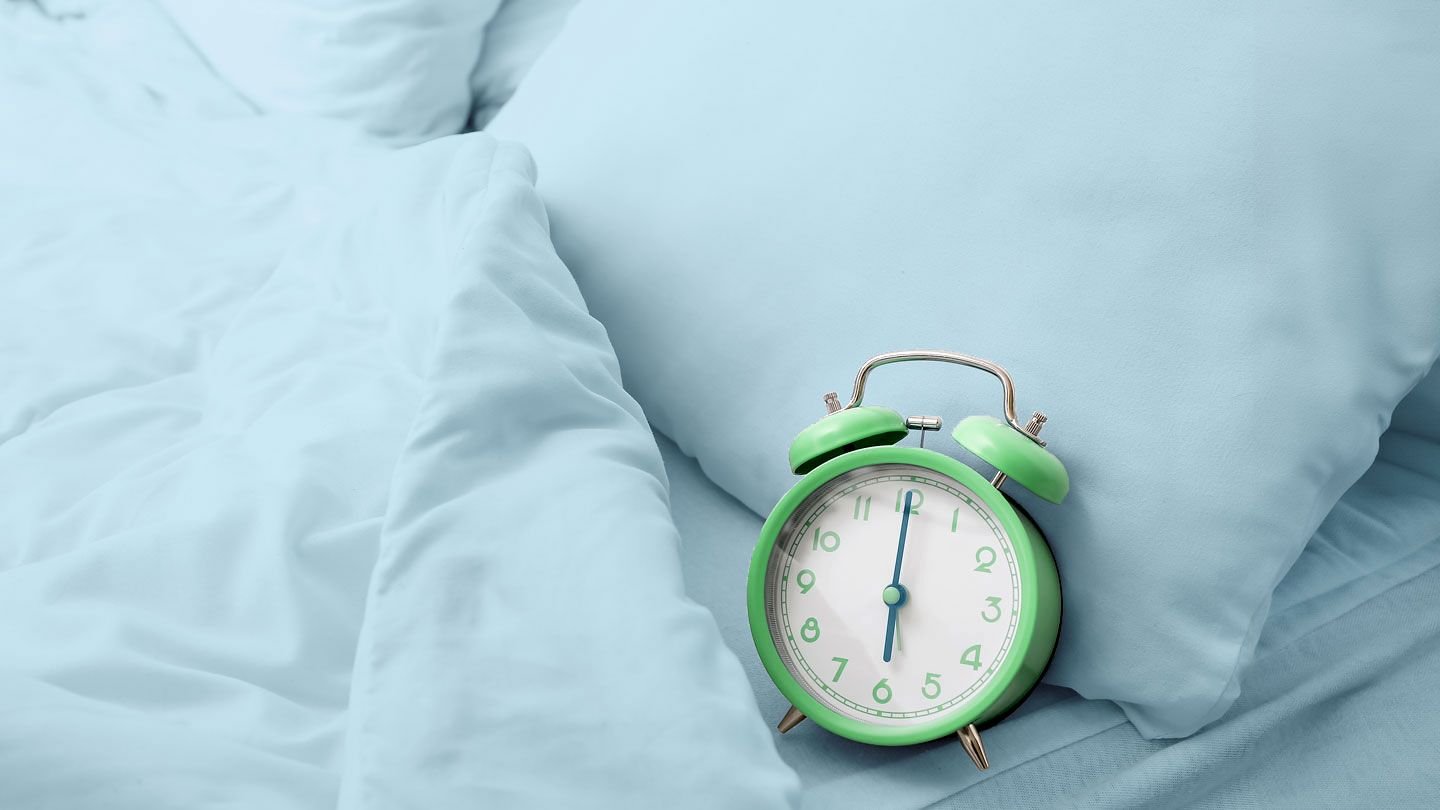 Green alarm clock on a bed with light blue sheets and pillows.