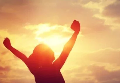 Silhouette of a person with arms raised against a sunset or sunrise sky.