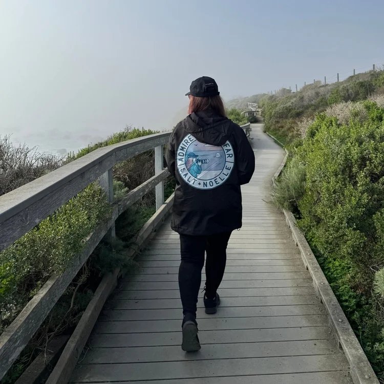 Alexis Noelle Galasso walking the boardwalk at the San Simeon elephant seal vista point in a Salt + Noelle Admire from Afar jacket.
