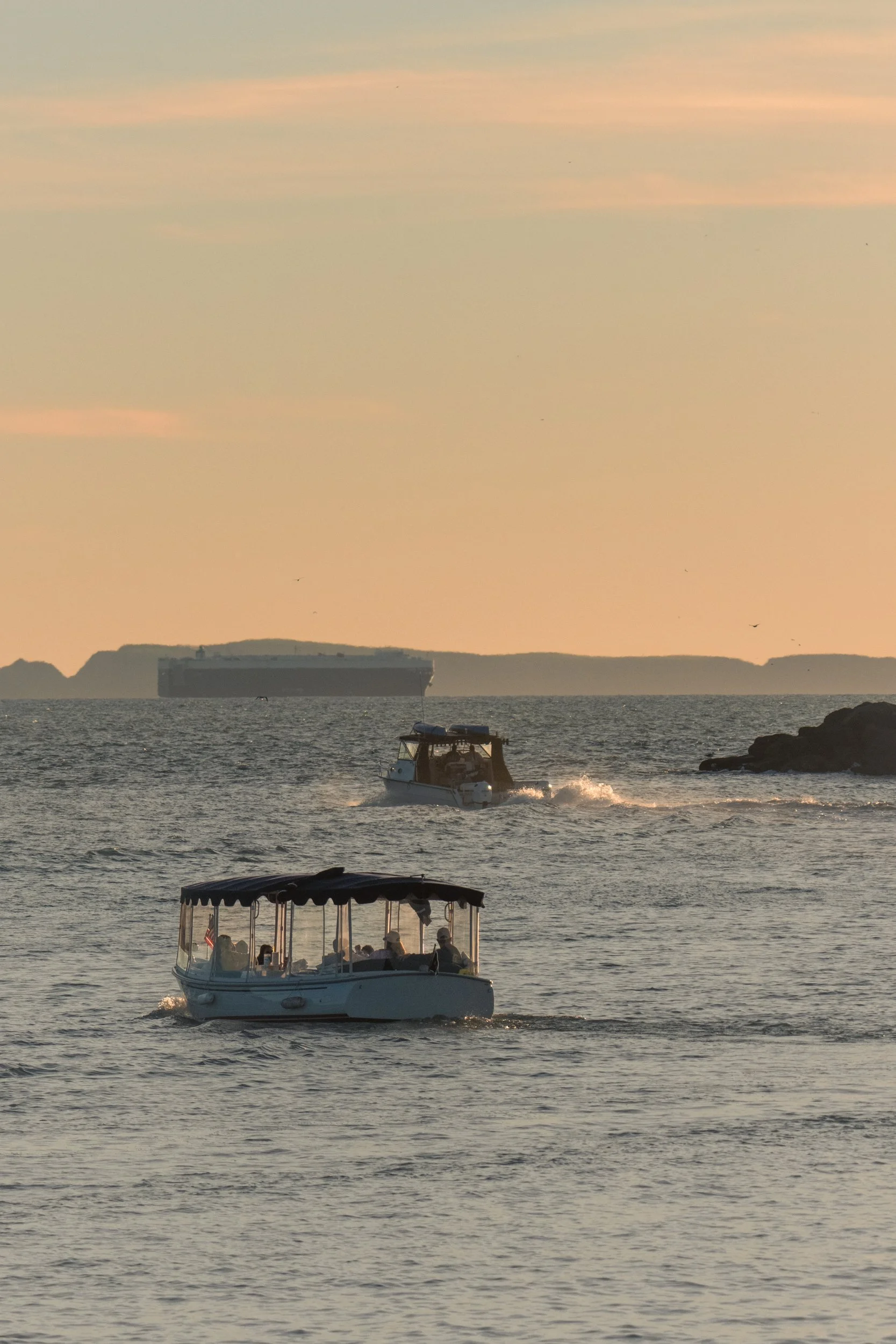 Two boats sailing on calm water with an island in the background during sunset or sunrise.