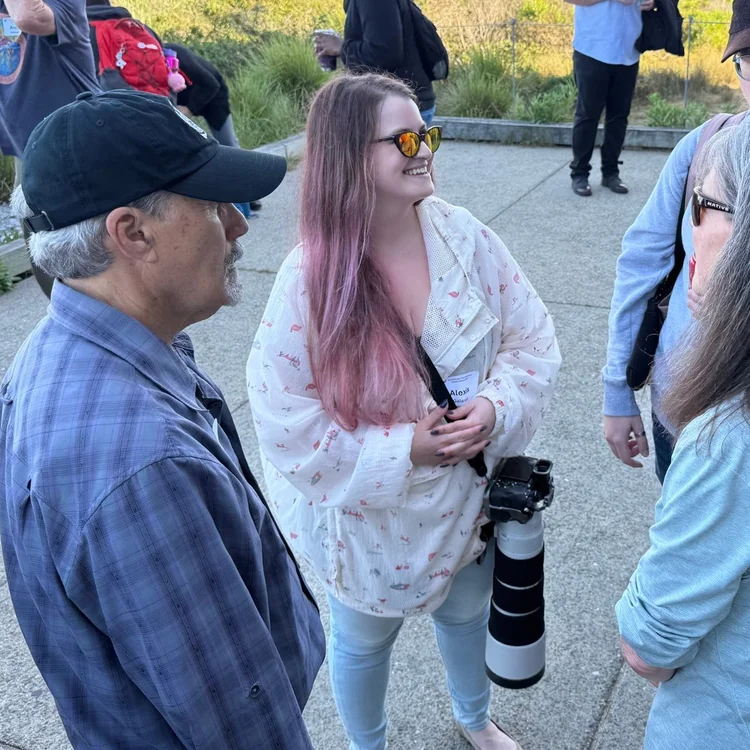 Alexis Noelle Galasso in conversation with colleagues at an outdoor gathering on the coast.