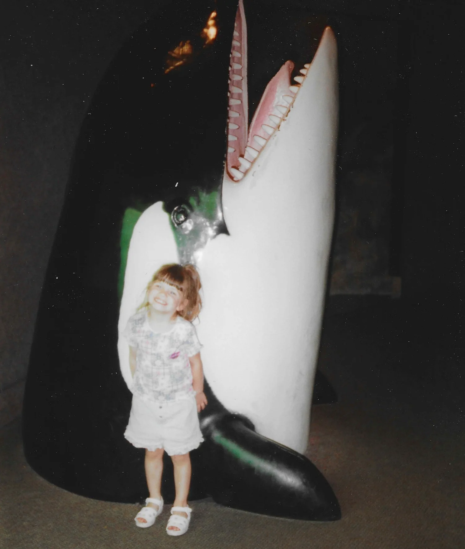Alexis as a child standing in front of an orca statue at the New York Aquarium on the Coney Island boardwalk in Brooklyn.