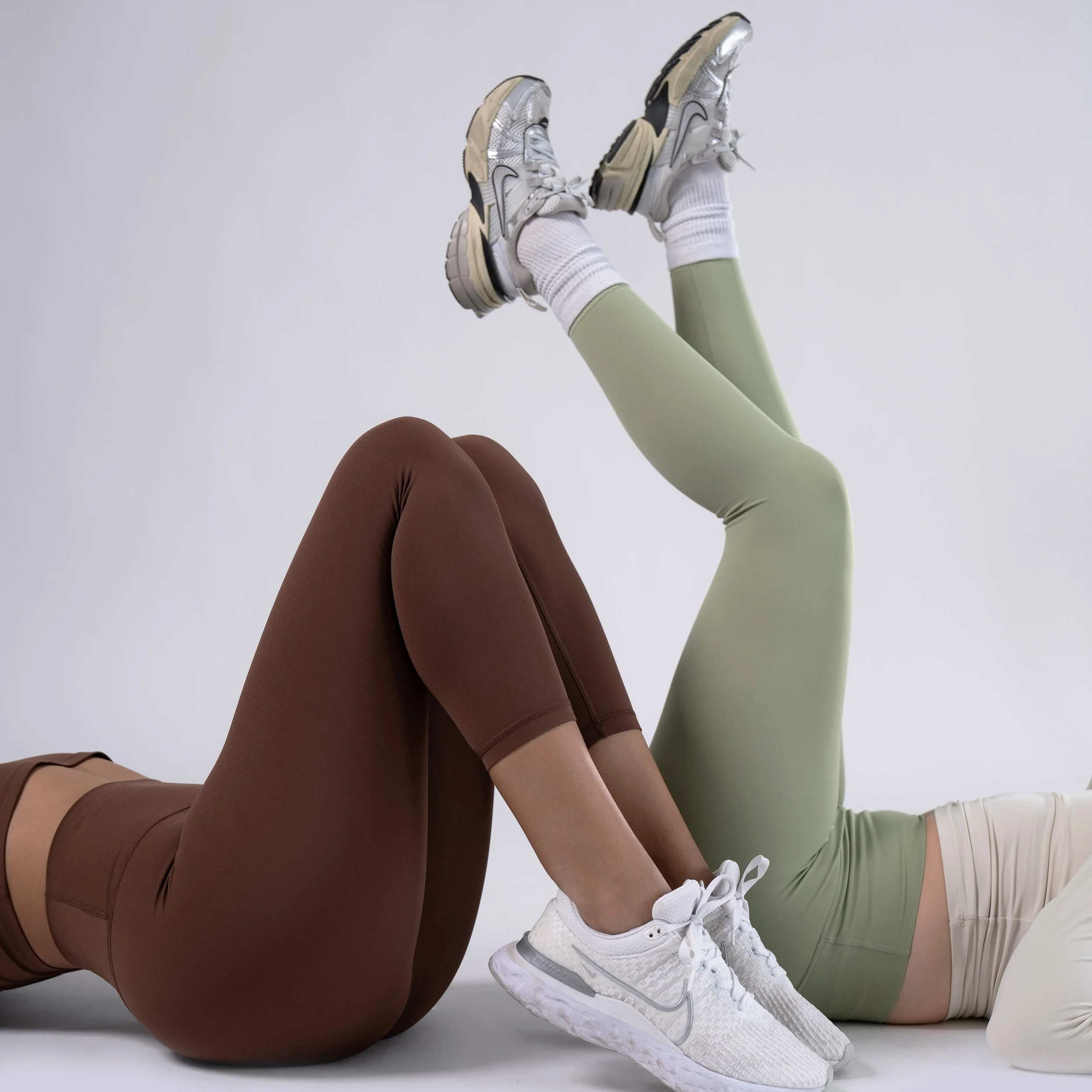 Two individuals lying on the ground with their Bask Body UPF 50 leggings and sneakers on, against a plain background.