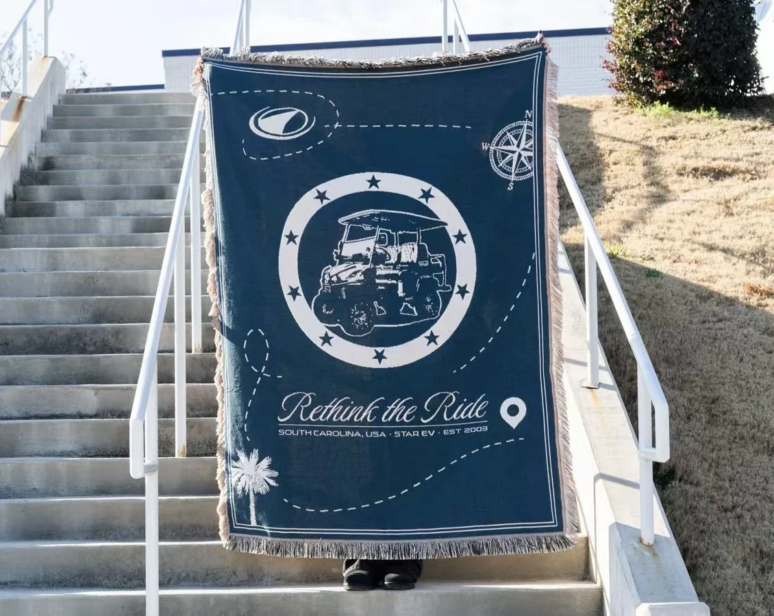 A large blue fabric banner hanging on stairs with a golf cart illustration surrounded by stars, a palm tree, and a compass, with the text "Rethink the Ride" and "South Carolina, USA - STAR EV - EST 2003".