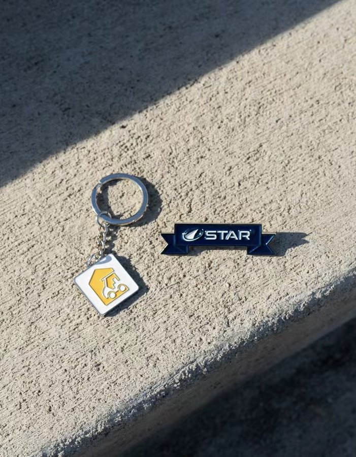A keychain with a yellow mechanical helmet charm and a pin with the logo and name 'Star' resting on a concrete surface.