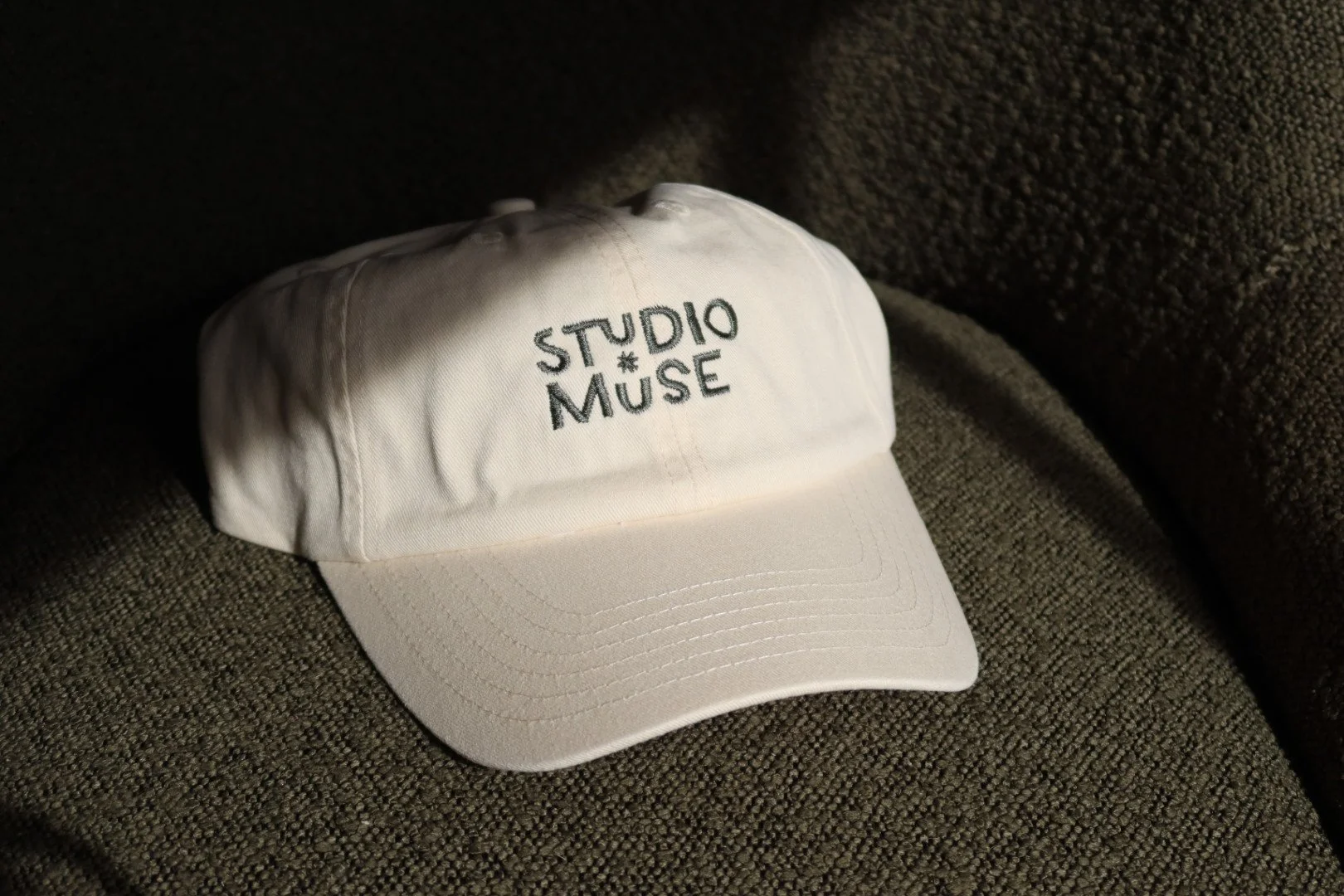 A picture of a beige hat with studio muse embroidered onto the front in dark green