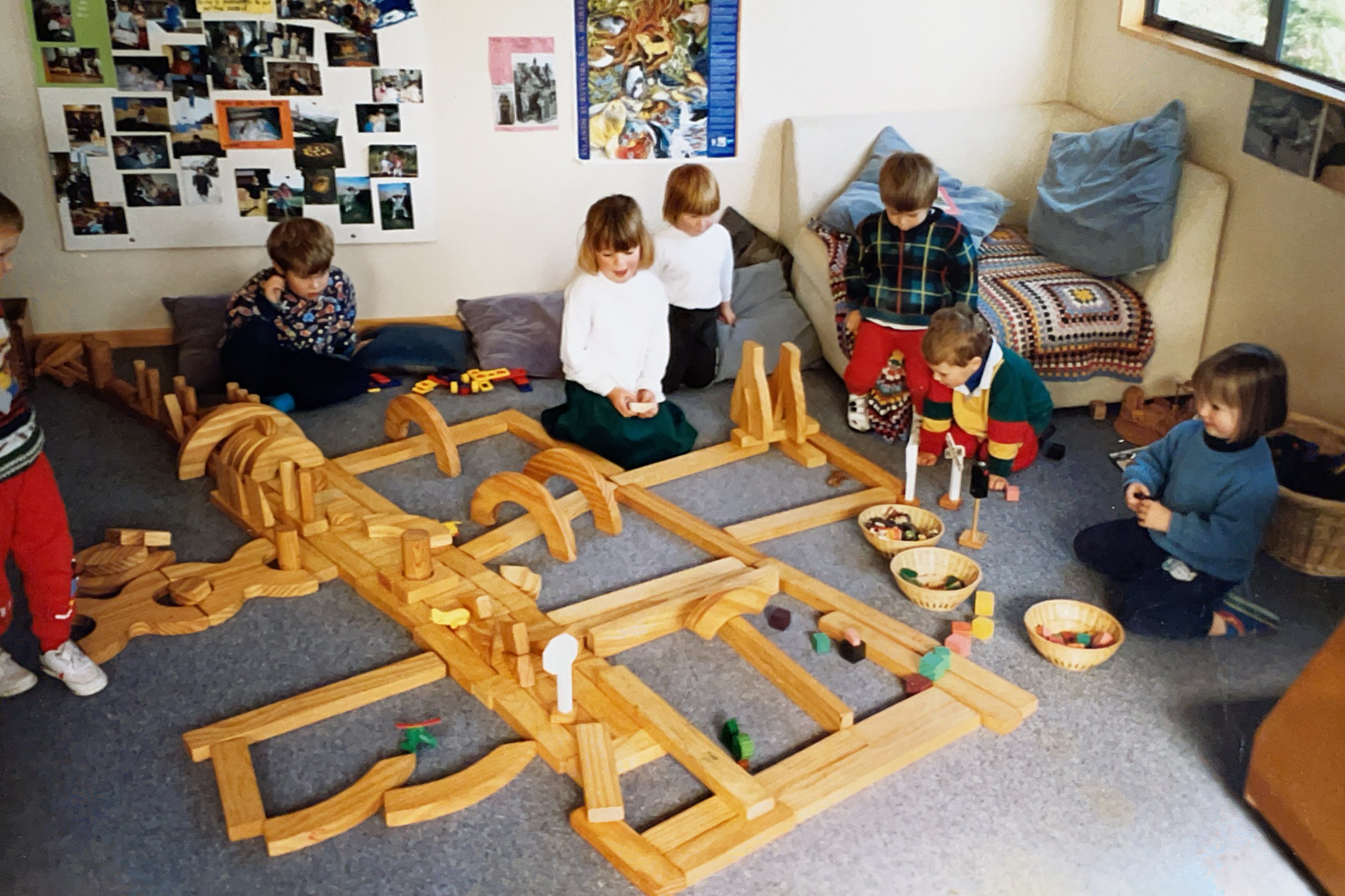 Children playing with wooden train tracks and toys in a cozy indoor playroom.