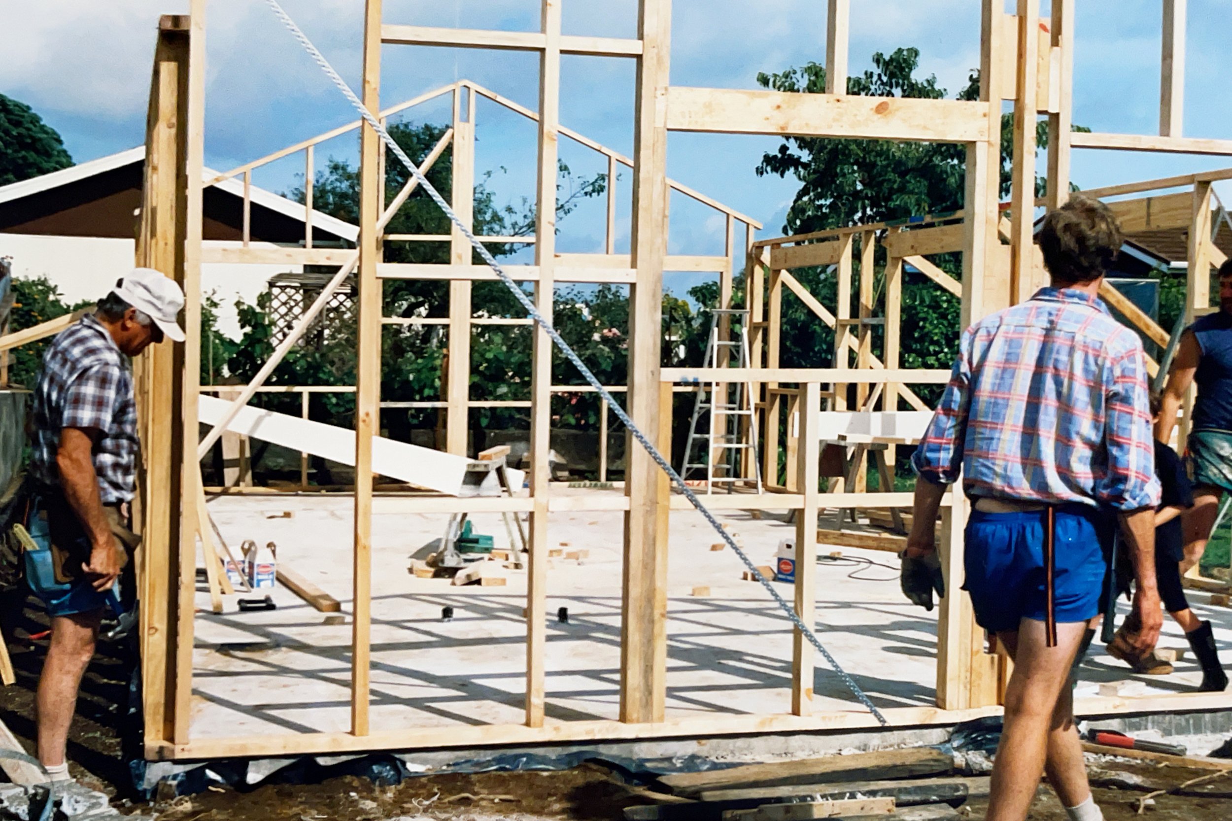 Construction workers building a wooden house framework outdoors on a bright day.