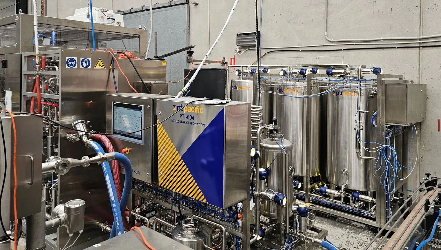 Industrial machine labeled 'PTI-604 Molecular Carbonation' with pipes, tubes, tanks, and a digital control screen in a factory setting.