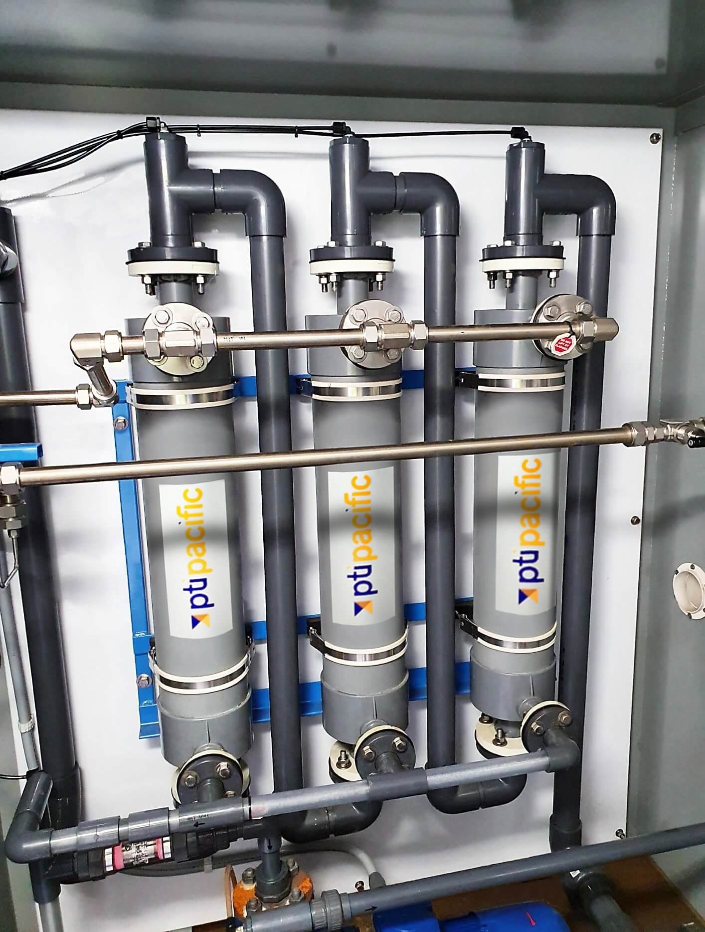 Industrial water filtration system with three vertical gray filters labeled 'pt pacific', connected by black, blue, and gray pipes.