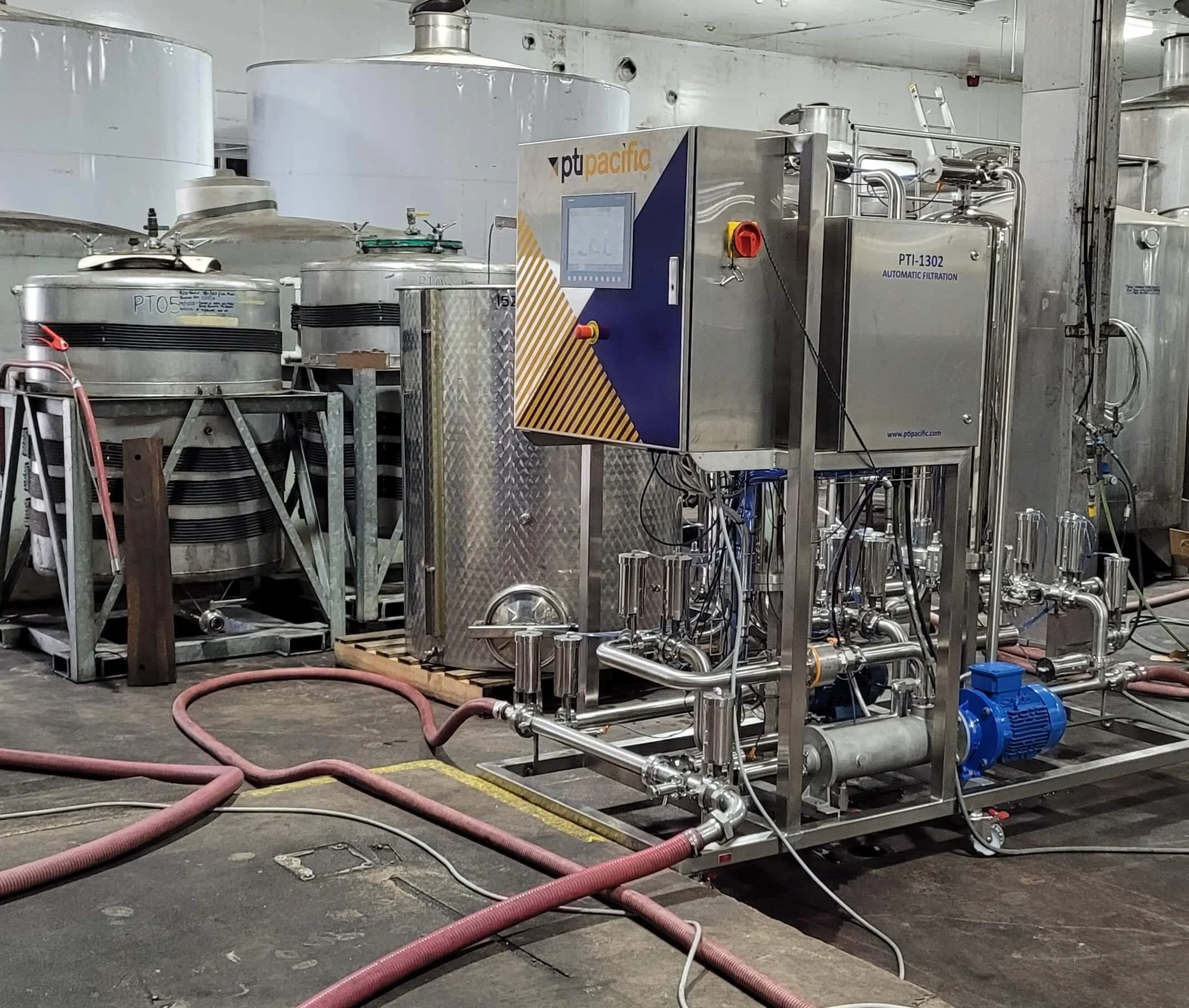 Industrial water filtration system with stainless steel components, pipes, and hoses in a factory setting.