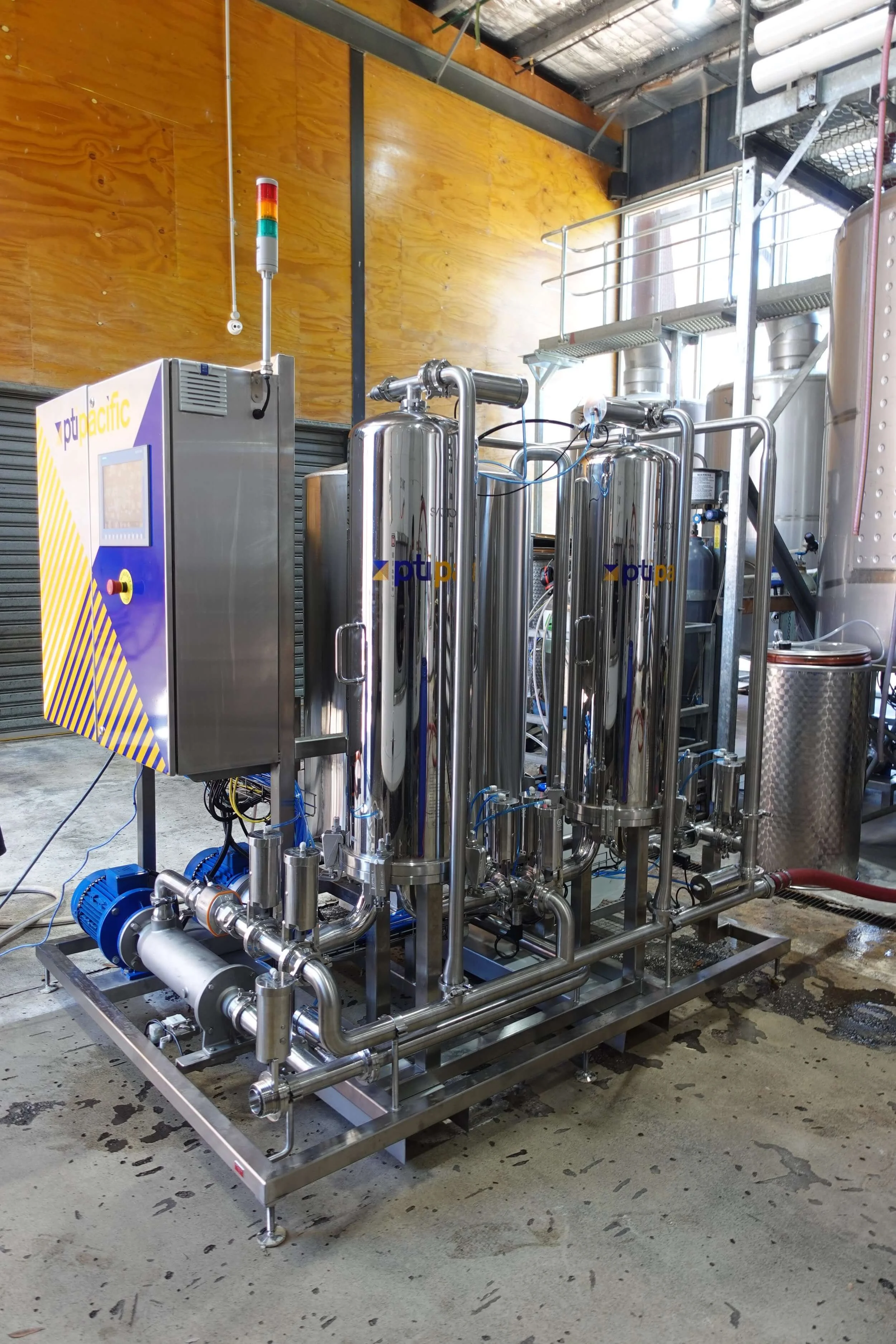 Industrial water filtration system with stainless steel cylinders, pipes, and a control panel on a metallic frame.