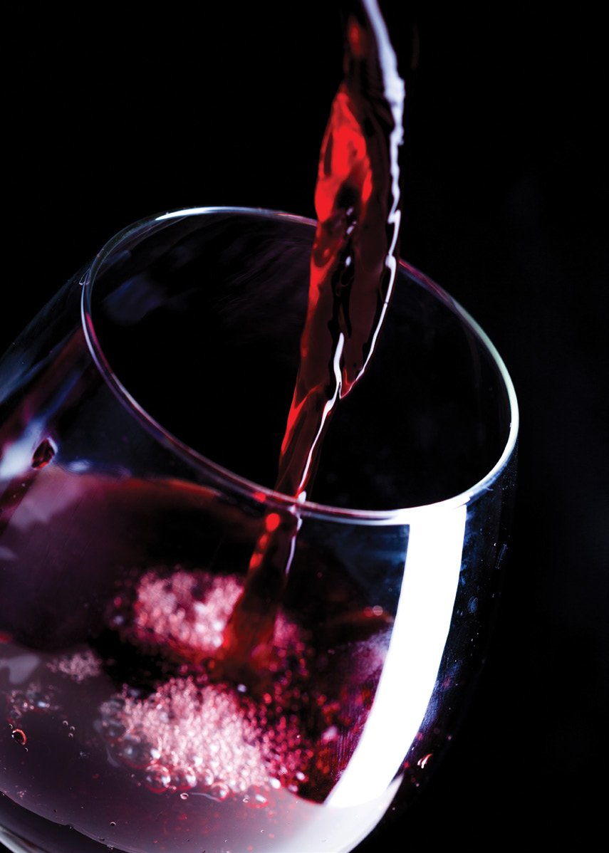 Red wine being poured into a glass against a dark background.