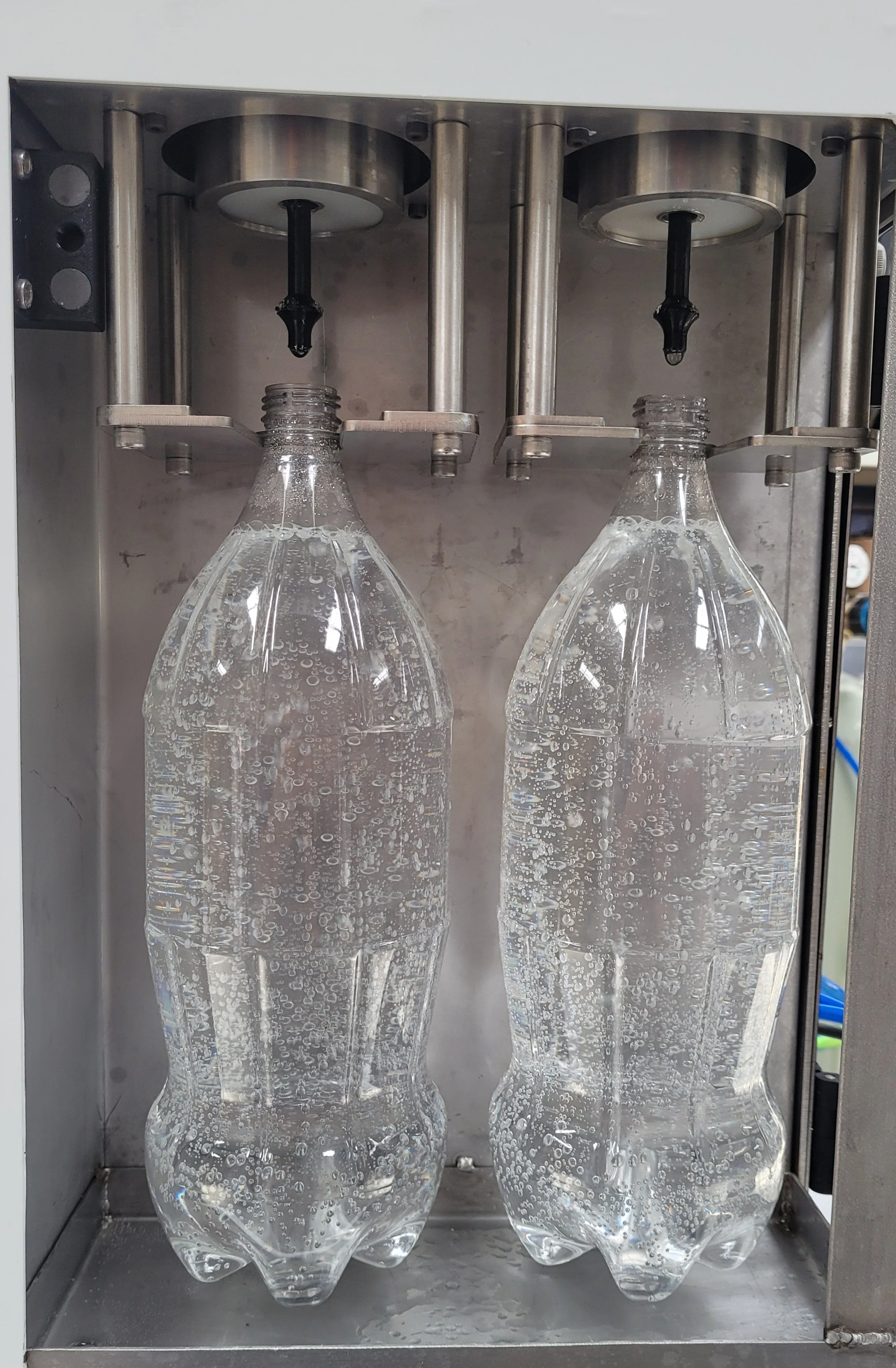 Two plastic bottles are being filled with carbonated water from a machine dispenser.