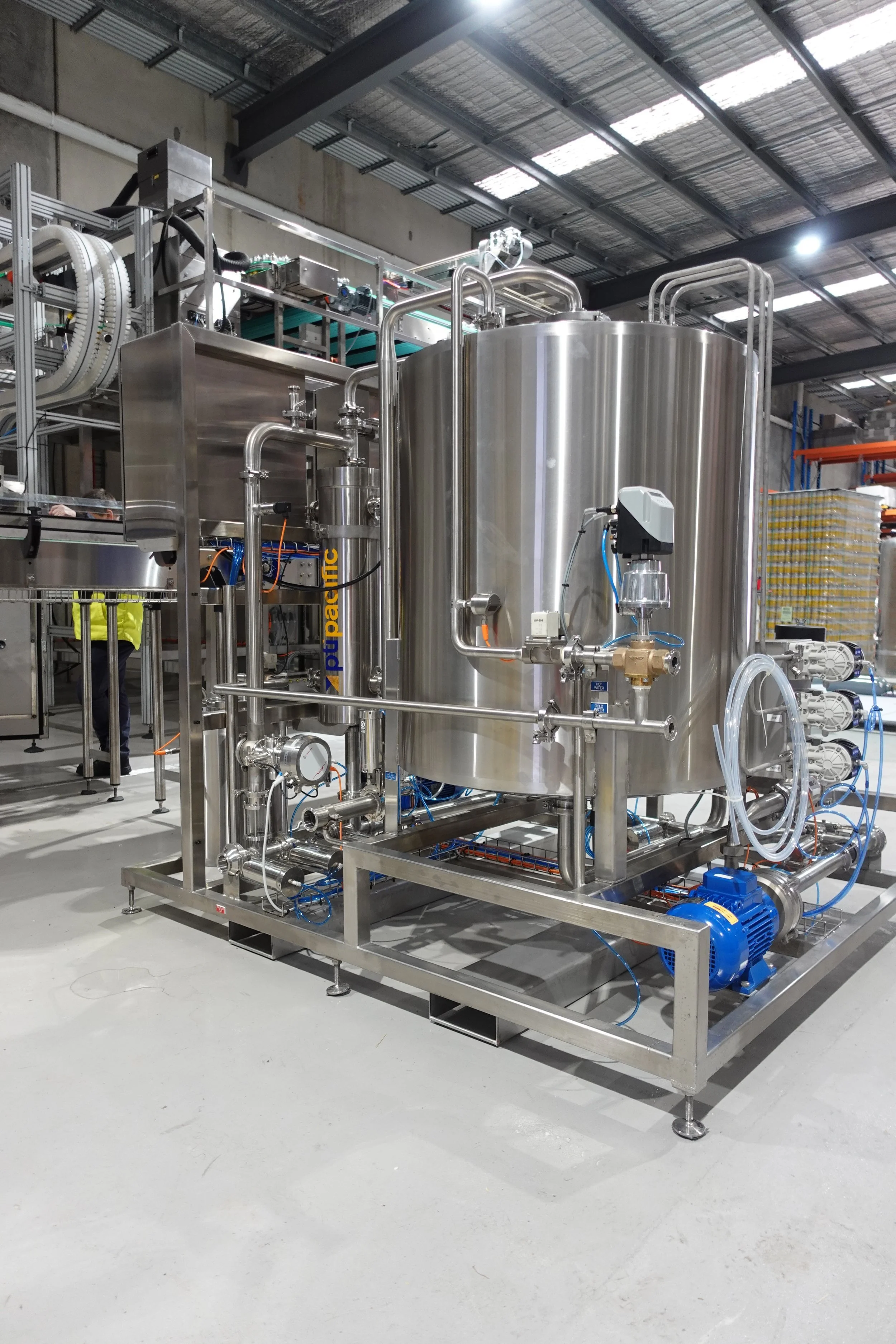Industrial stainless steel tank with pipes and machinery in a factory setting.