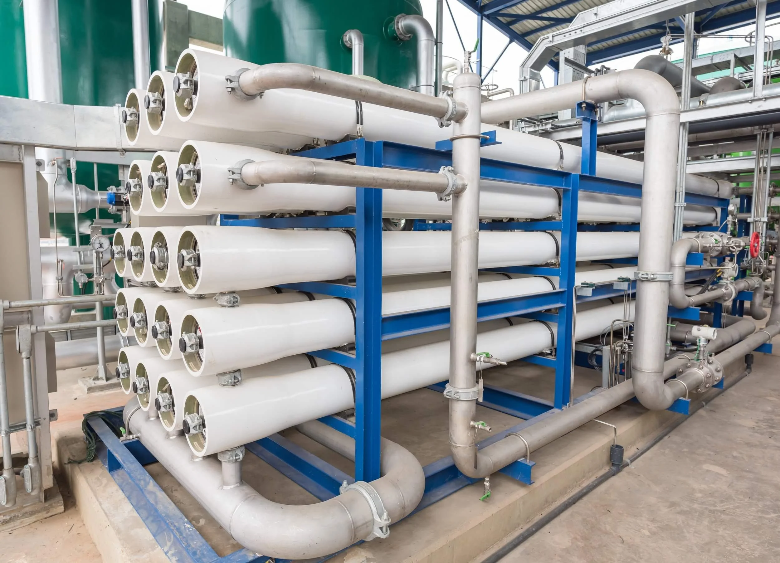 Industrial water filtration system with multiple white cylindrical filters mounted on a blue frame, connected by gray pipes and valves.