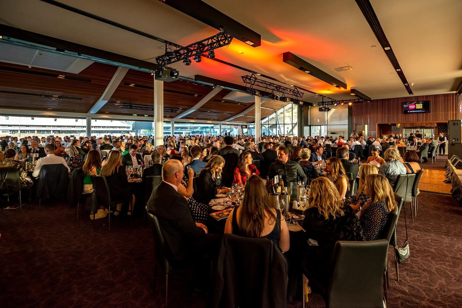 A large group of people seated at tables in a spacious, elegantly decorated event hall during a formal gathering or banquet.