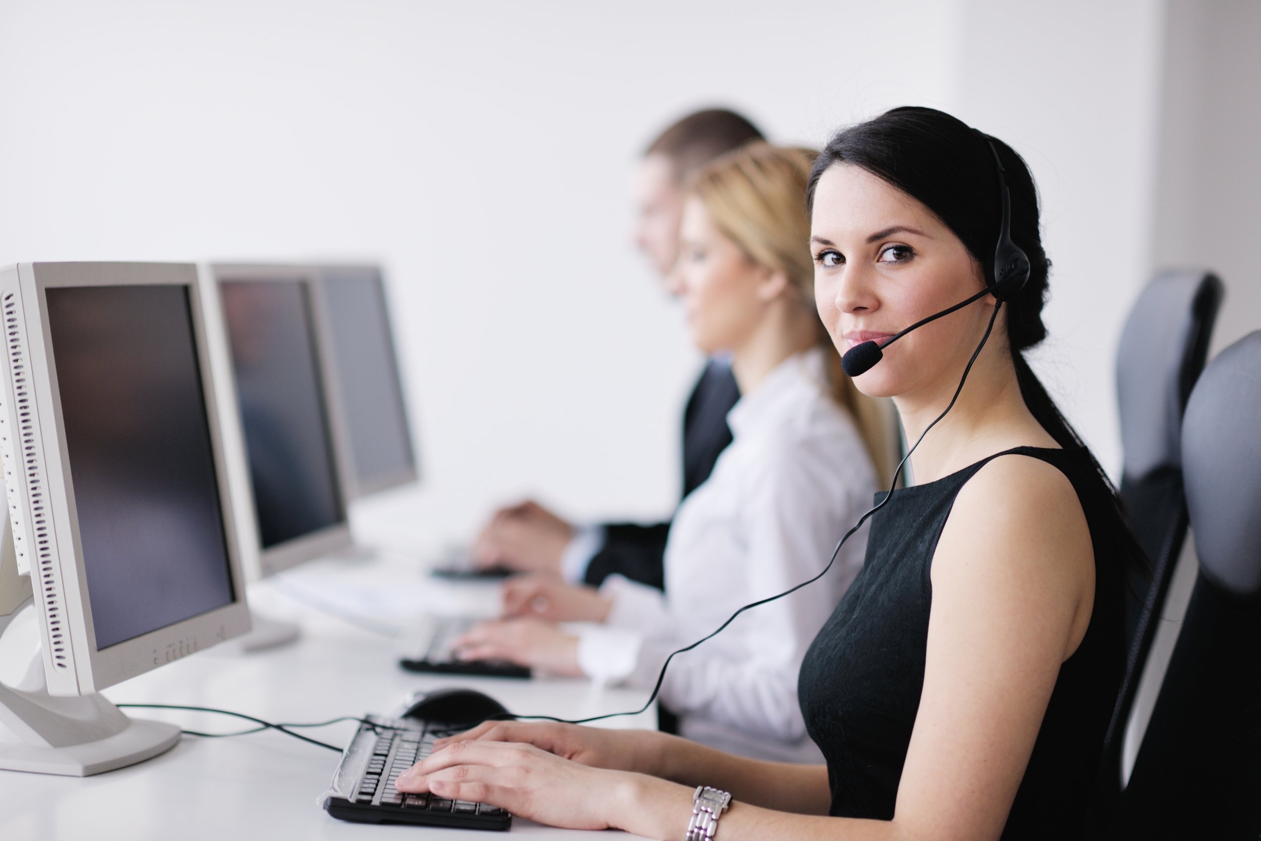 Customer service representatives with headsets working on computers in a call center.