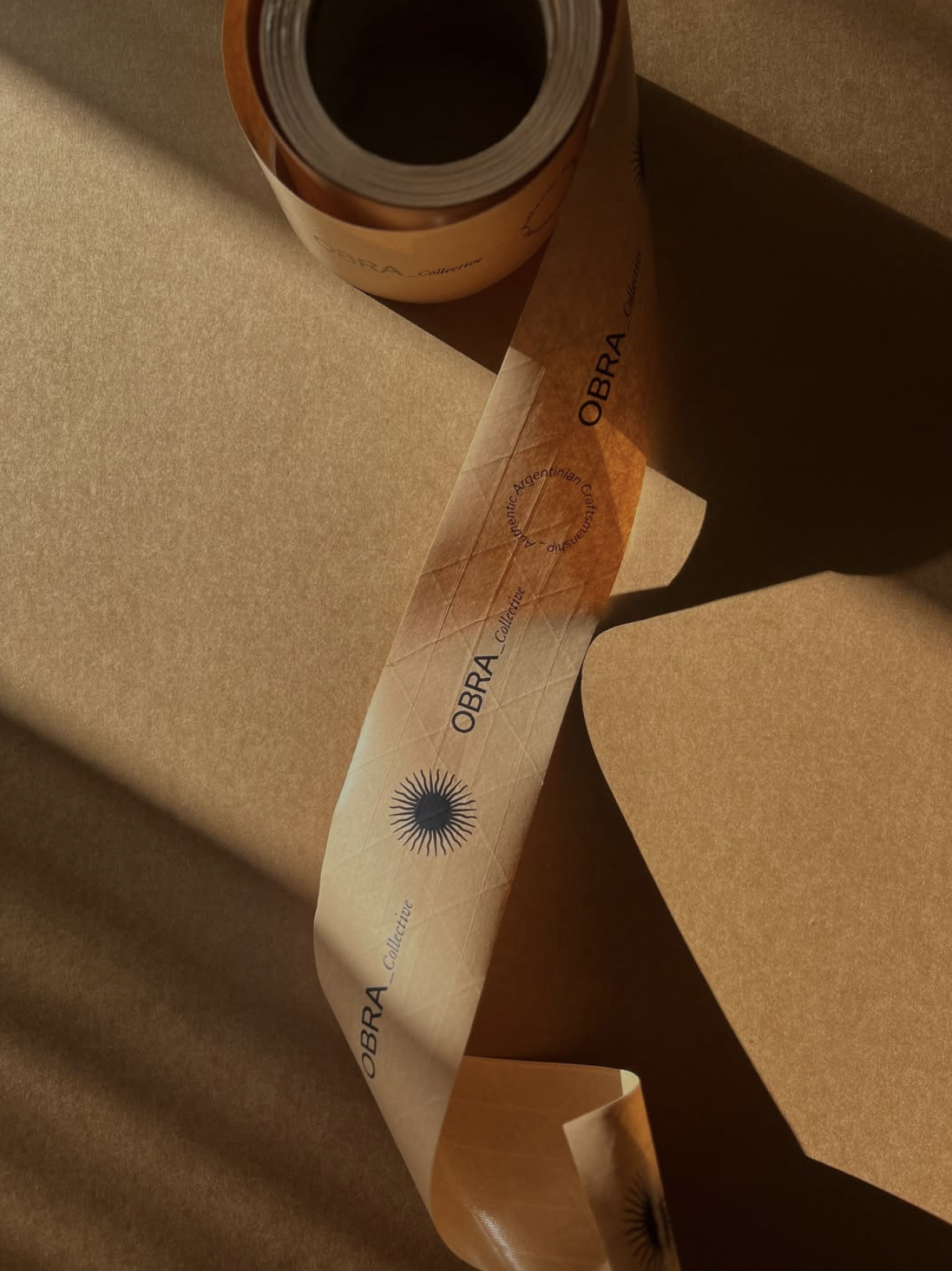 Kraft-finish water-activated tape with Obra Collective logo sealing a recycled Kraft box, showcasing sustainable packaging and eco-friendly shipping.
