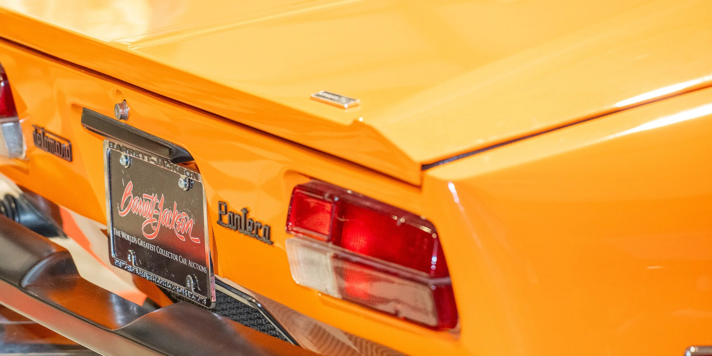 Close-up of the rear orange Pontiac Firebird Trans Am, showing the taillight, emblem, and a collector car auction license plate.
