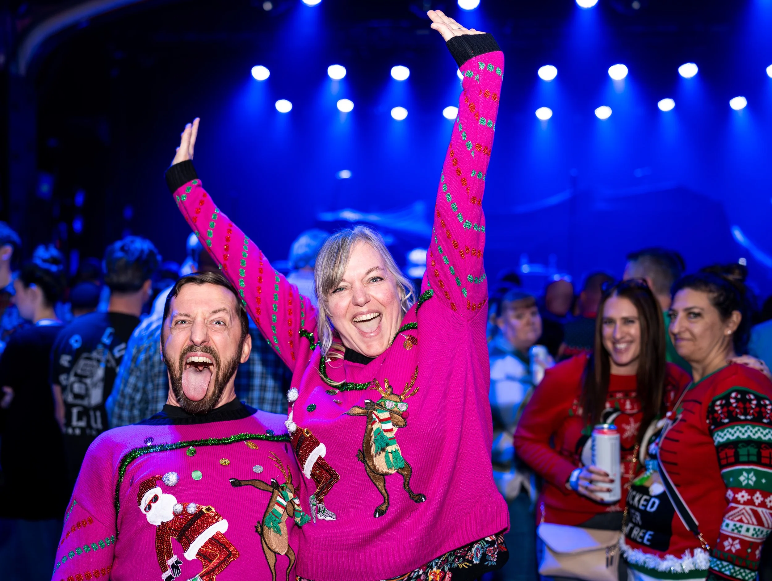 People celebrating at a festive event wearing colorful Christmas sweaters with holiday designs, smiling and enjoying the party.