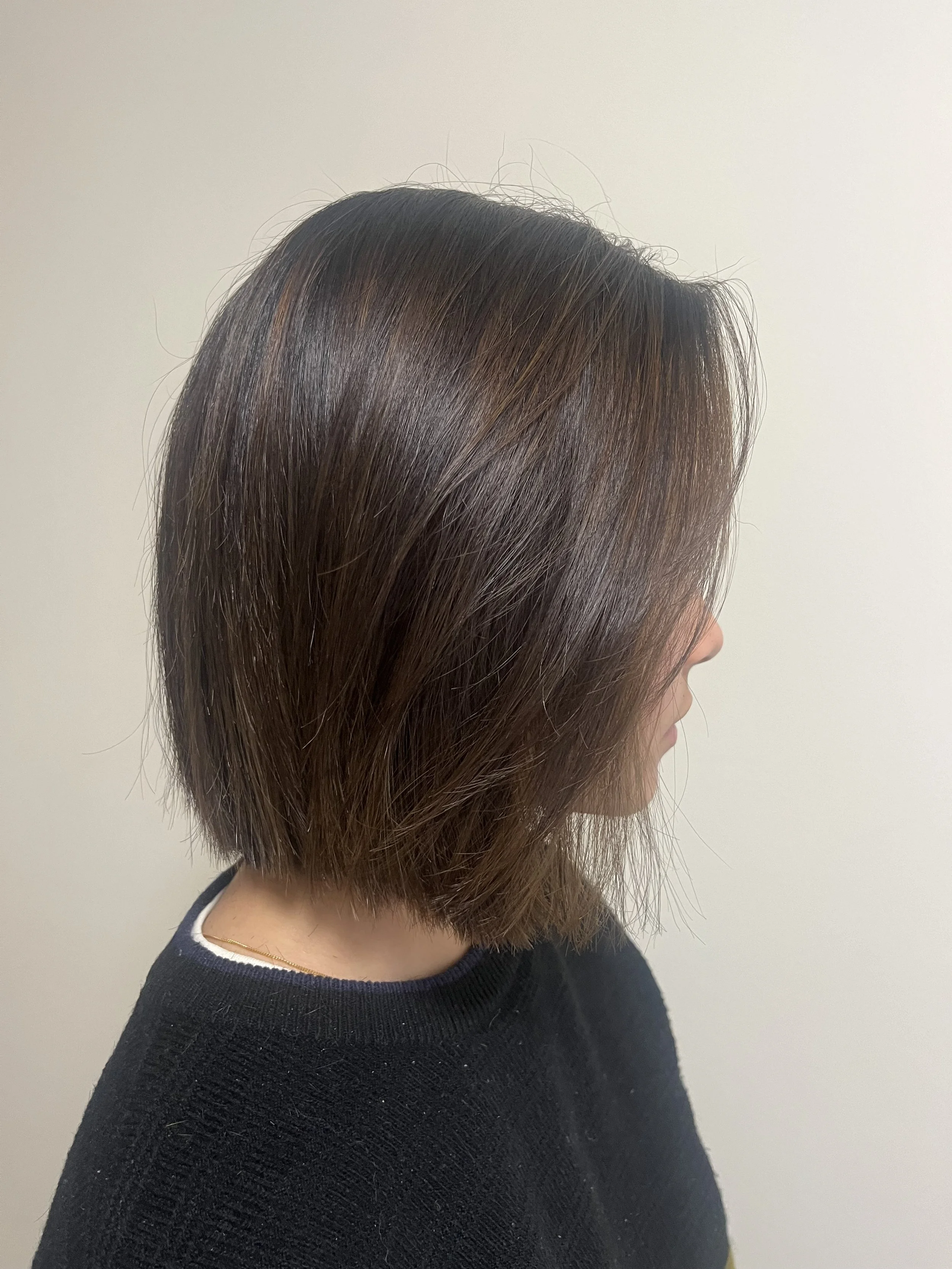 Profile view of a person with straight, shoulder-length brown hair wearing a black sweater.