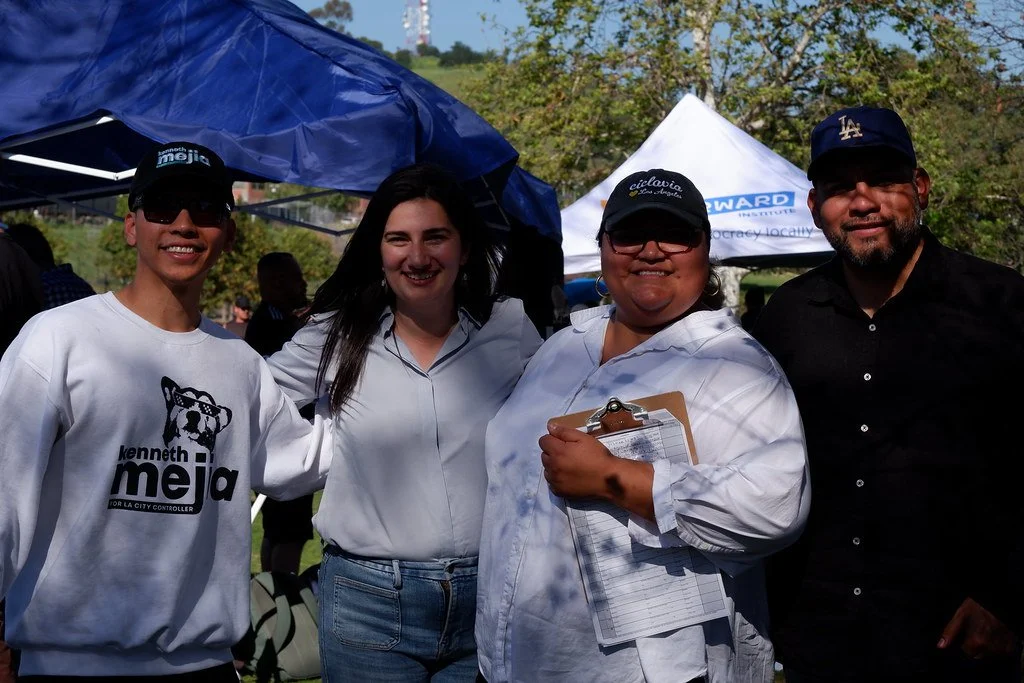 Four people standing outdoors at a festival or gathering, smiling, with tents in the background.