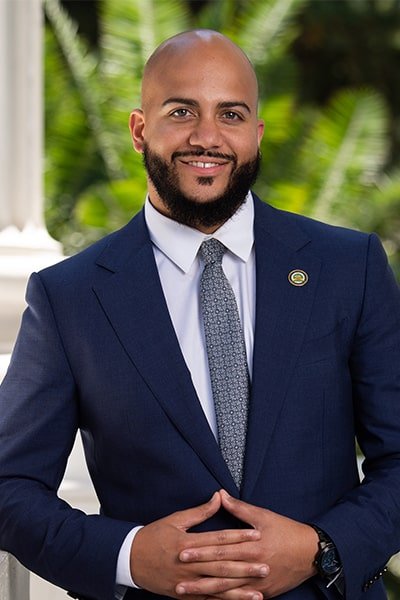 Endorsement of Isaac Bryan for Eunisses Hernandez. He is in a dark blue suit standing outdoors with green plants in the blurred background.