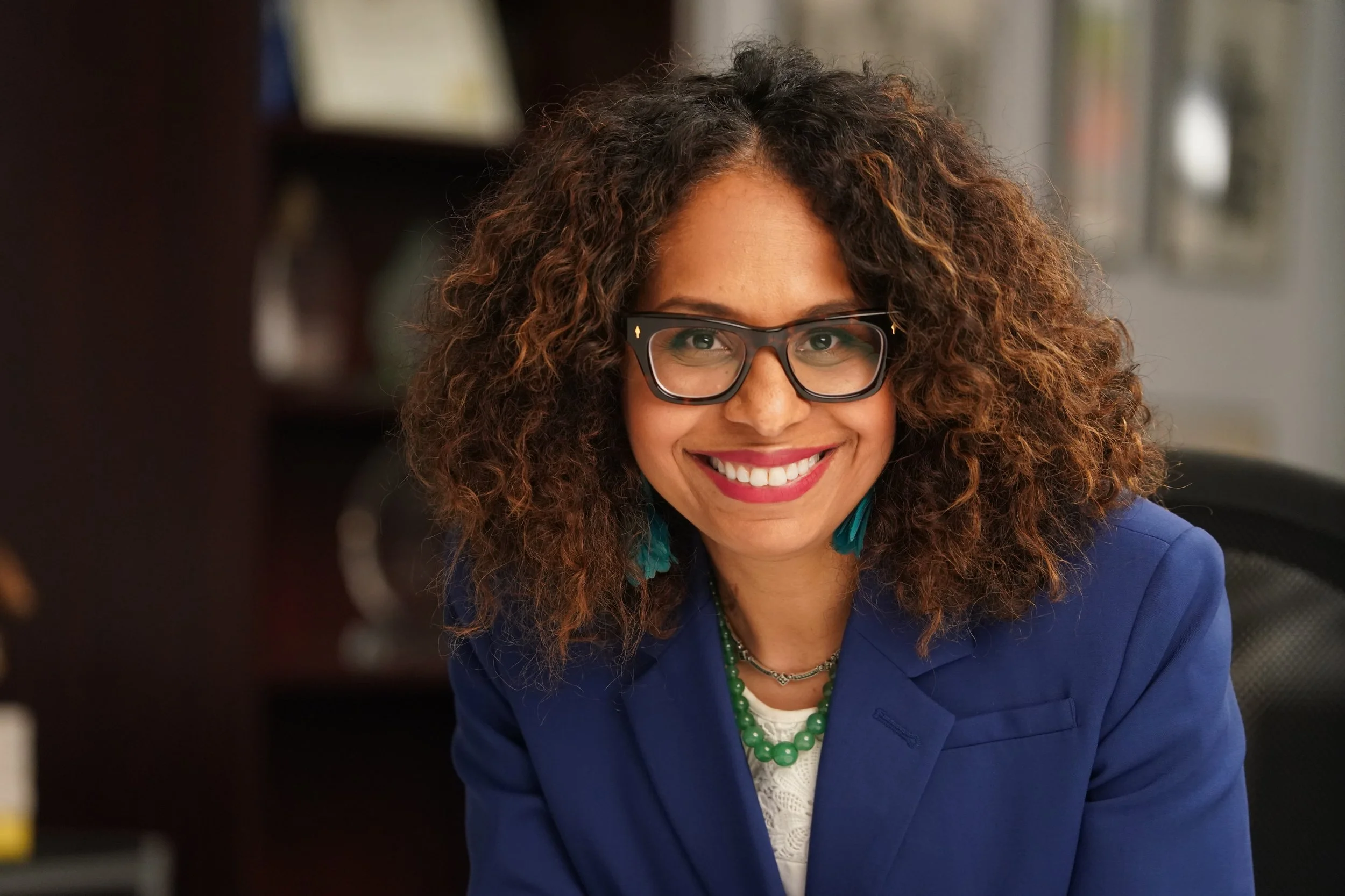 Endorsement of Sydney Kamlager-Dove for Eunisses Hernandez. She is wearing a navy blazer, white top, teal earrings, glasses, and a green beaded necklace in front of a blurred background.
