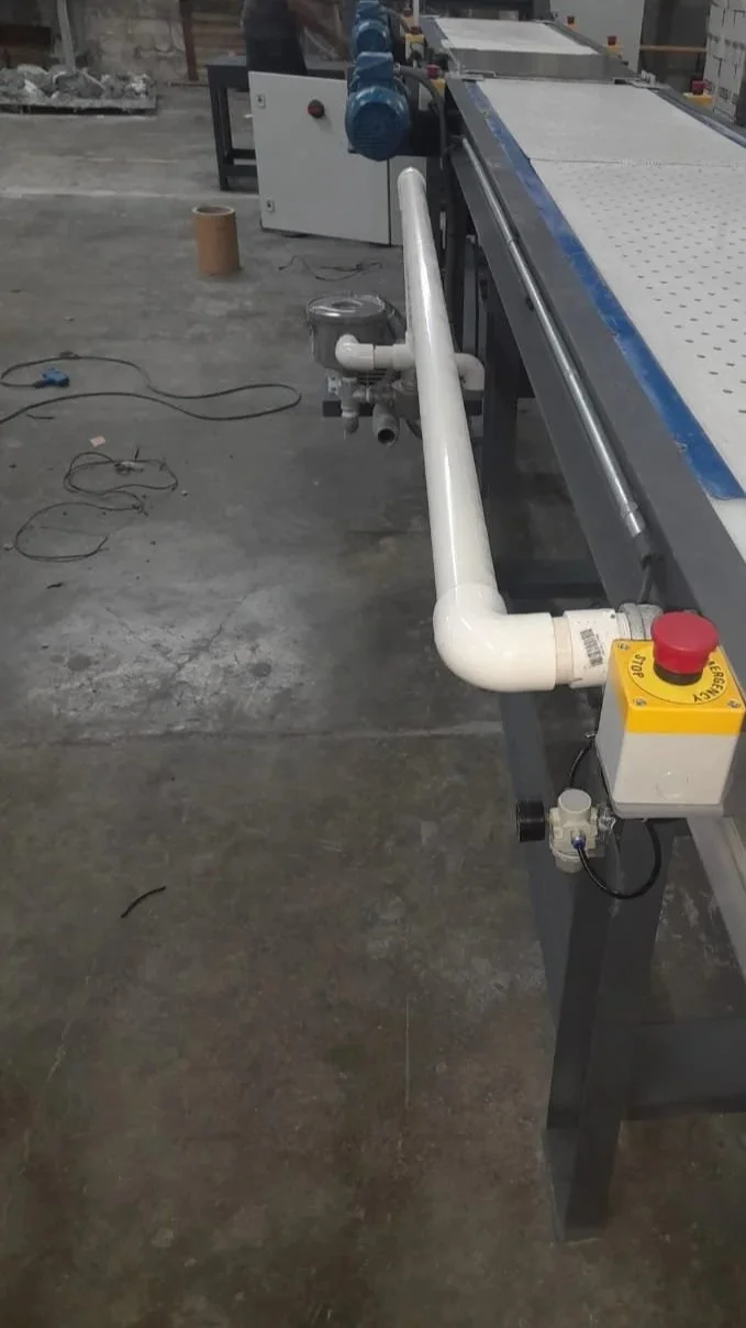 Tubería blanca conectada a una máquina industrial con control de emergencia rojo y amarillo en un entorno de fábrica.