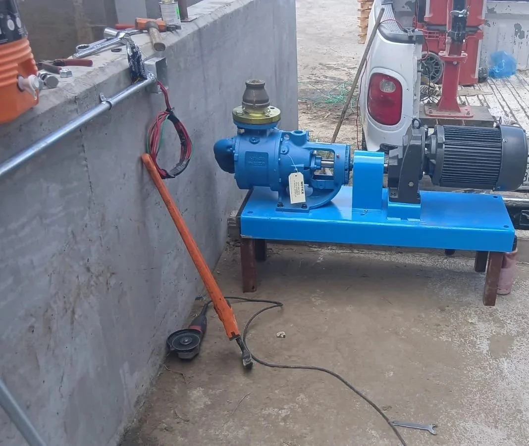 Equipo de bomba hidráulica en un sitio de construcción, con motor eléctrico conectado en una plataforma de metal, y herramientas y cables en el fondo.