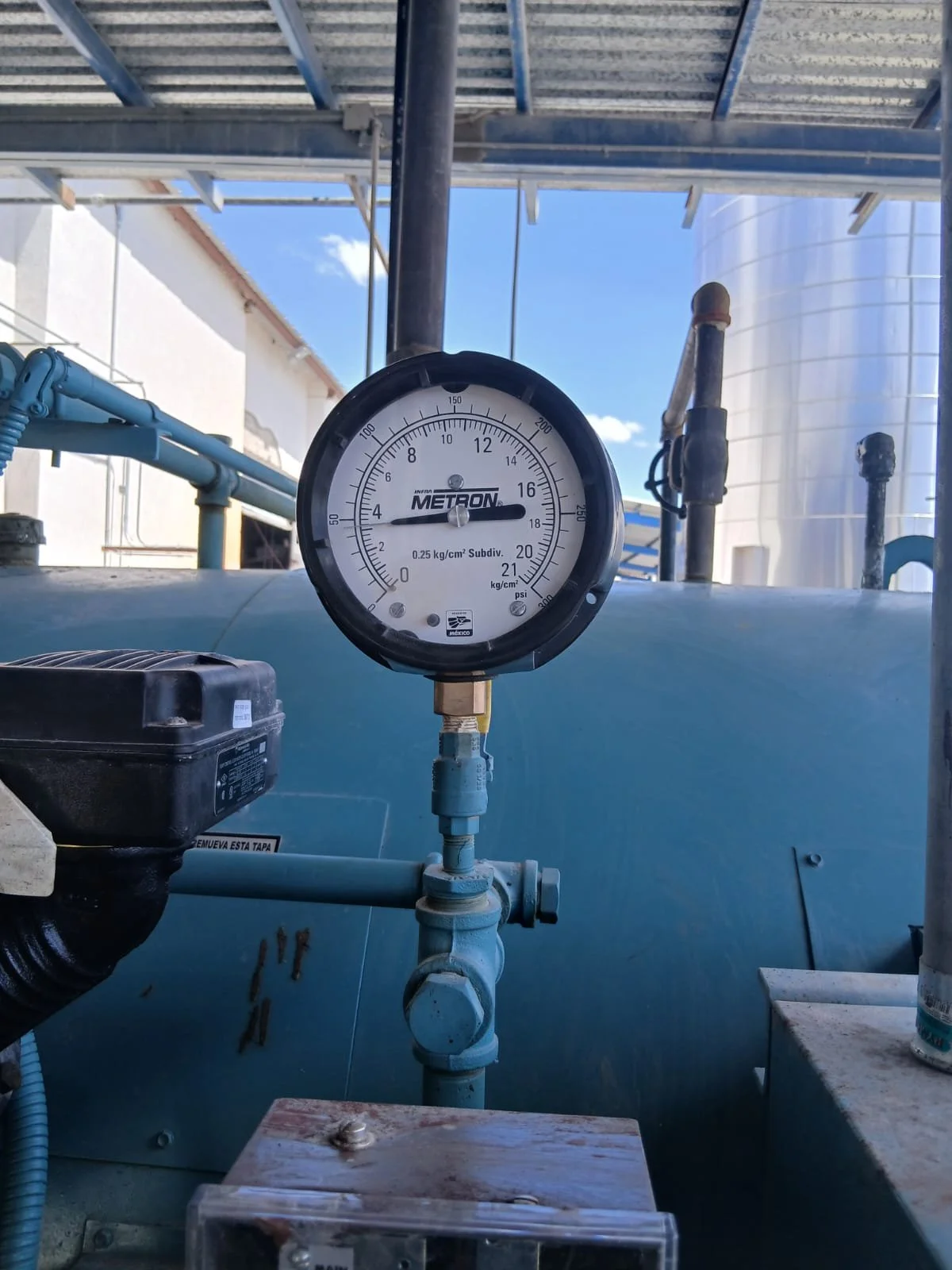 Manómetro en una tubería industrial, marca METRON, con lectura en 11 psi y 4 bar, en un entorno de plantas de procesamiento