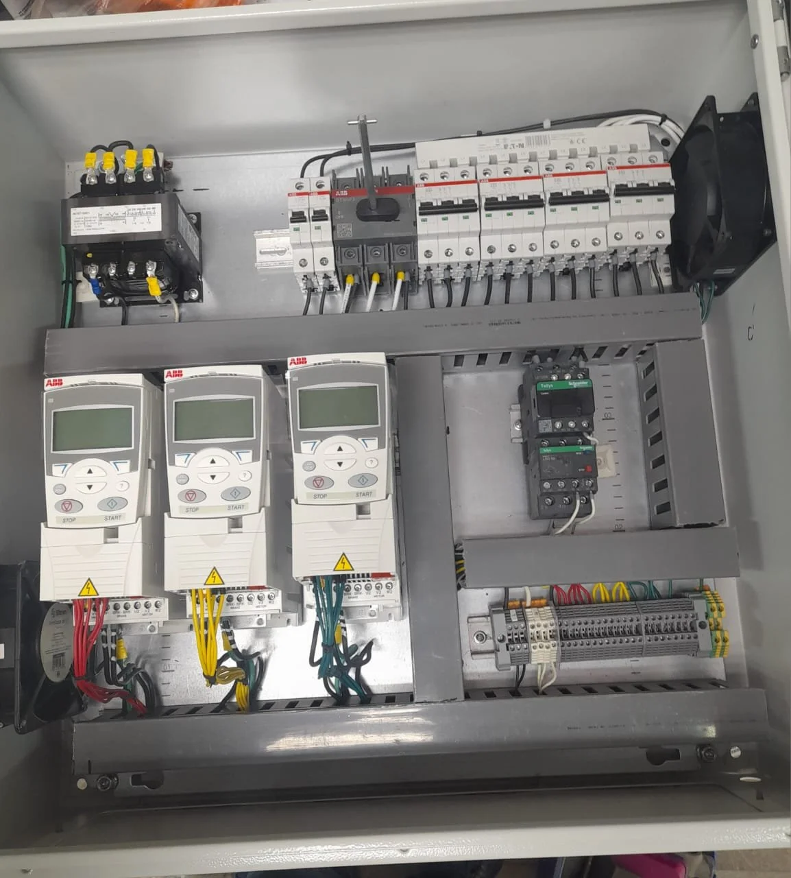 Tablero de control eléctrico con variadores de velocidad, disyuntores y componentes electrónicos en un gabinete metálico.
