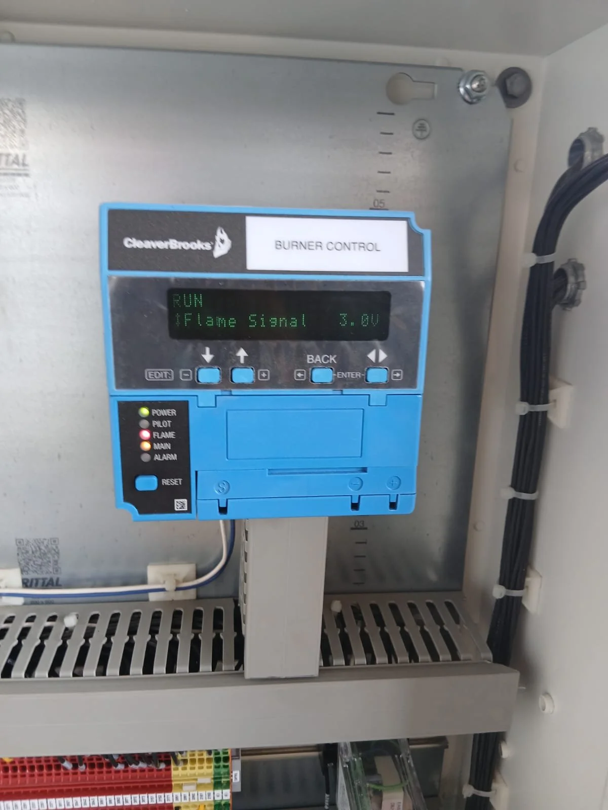 Controlador de quemador de incendios con pantalla digital que muestra 'RUN' y 'Flame Signal 3.0V', con luces verdes, amarillas y rojas indicando estado de potencia, piloto, llama, motor y alarma.