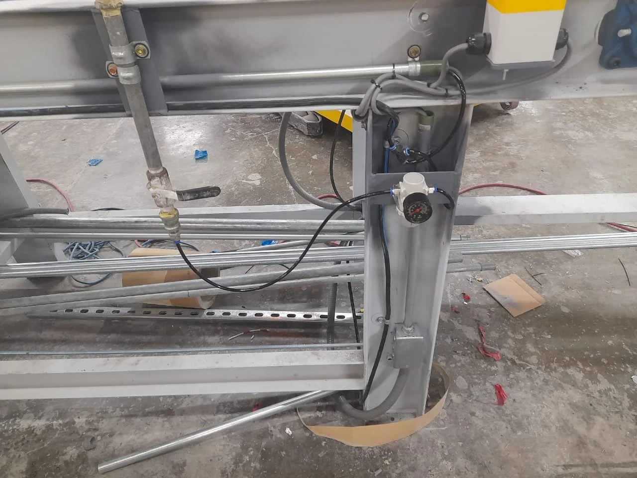 Equipo industrial metálico con tuberías, cables y conexiones en un entorno de taller o fábrica.