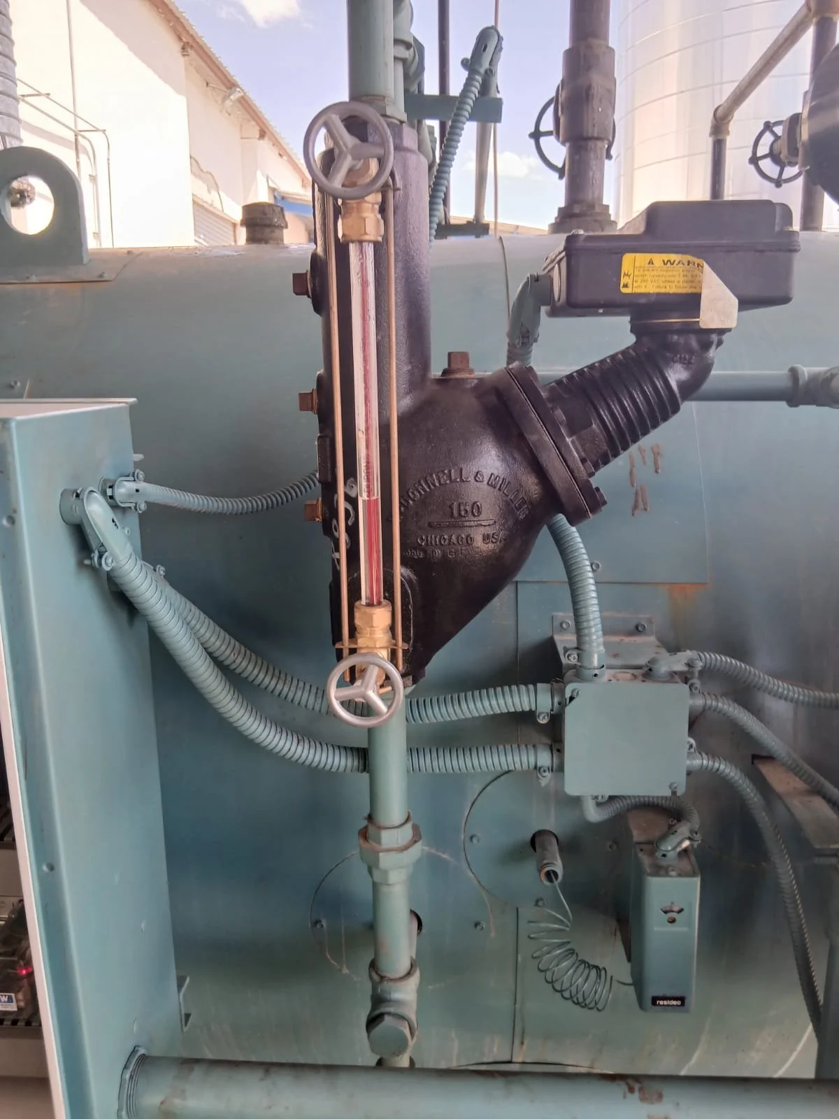 Sistema de tuberías y válvulas en una máquina industrial con un medidor de presión y cables eléctricos.